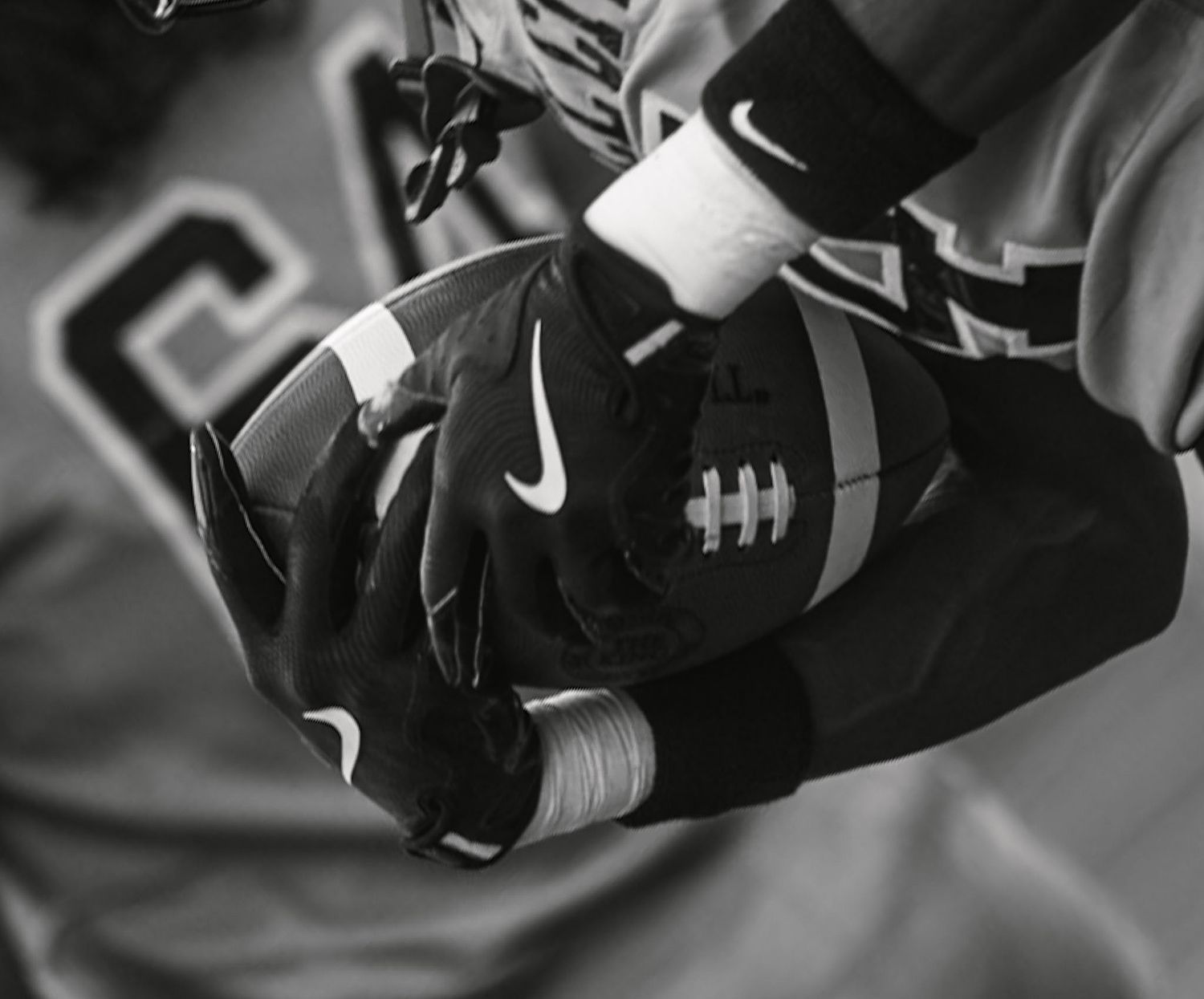 Player holding football with Nike gloves in black and white photo.