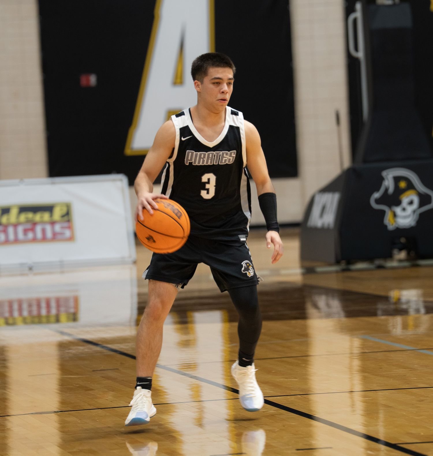 Basketball player number 3 in black Pirates uniform dribbles ball on indoor court.