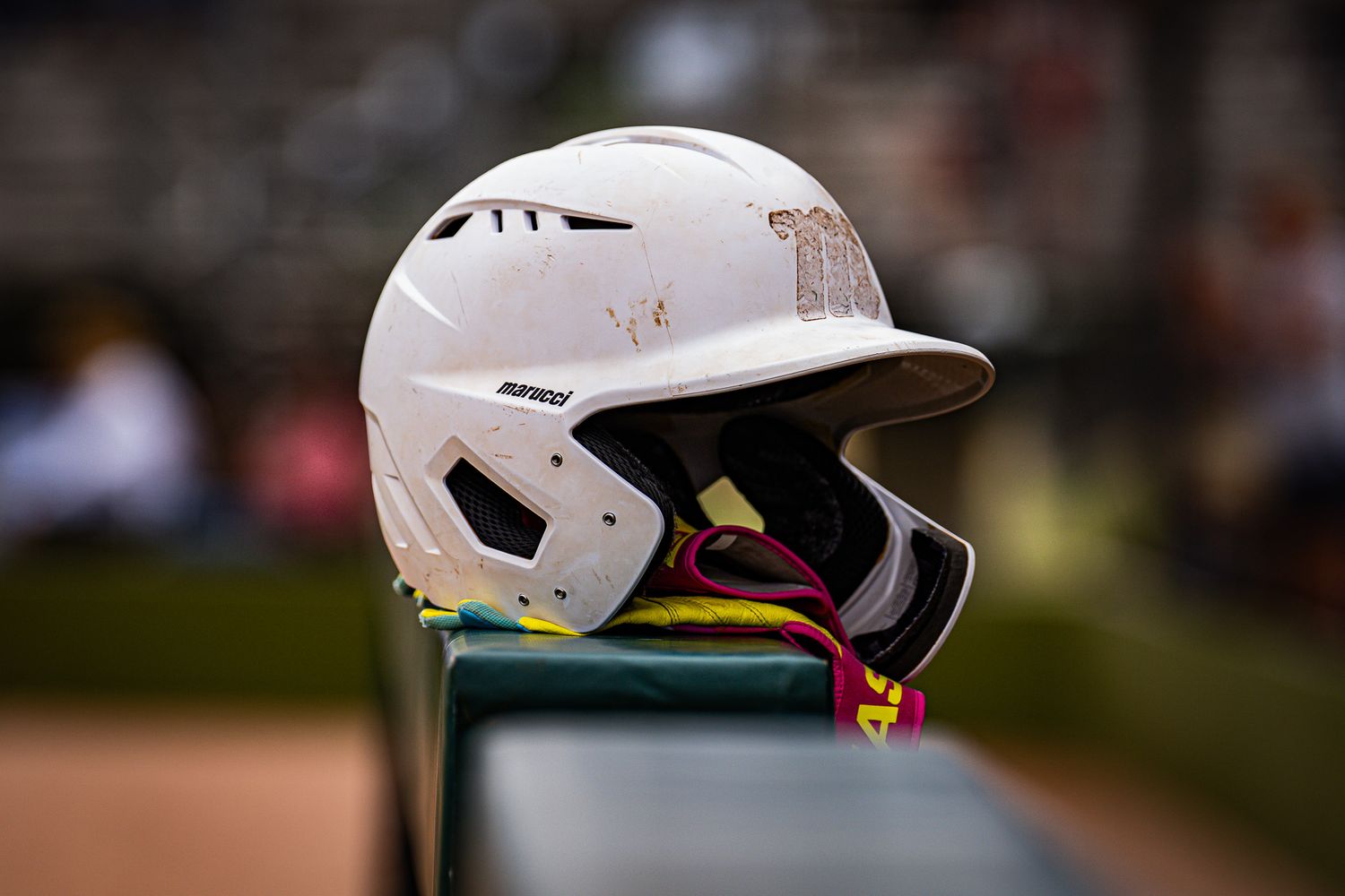 A white batting helmet with face guard sits on a dugout ledge during a baseball game.