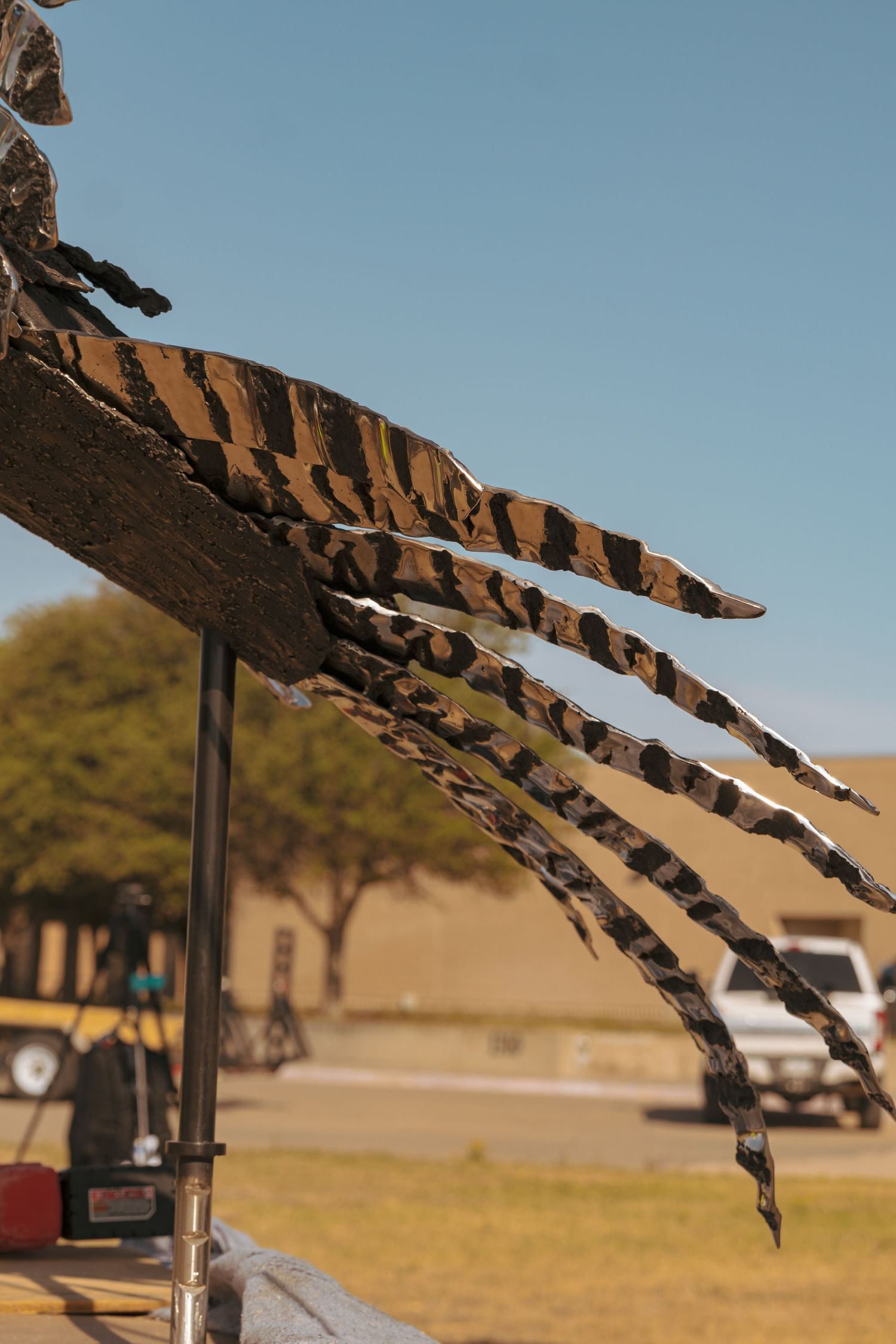 Close-up of striped metal feathers on a large bird sculpture against a clear blue sky.