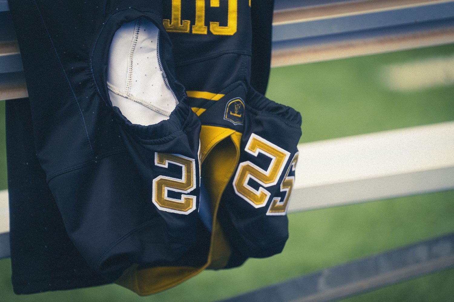 Navy and gold football jerseys with number 25 hanging on stadium bench railing.
