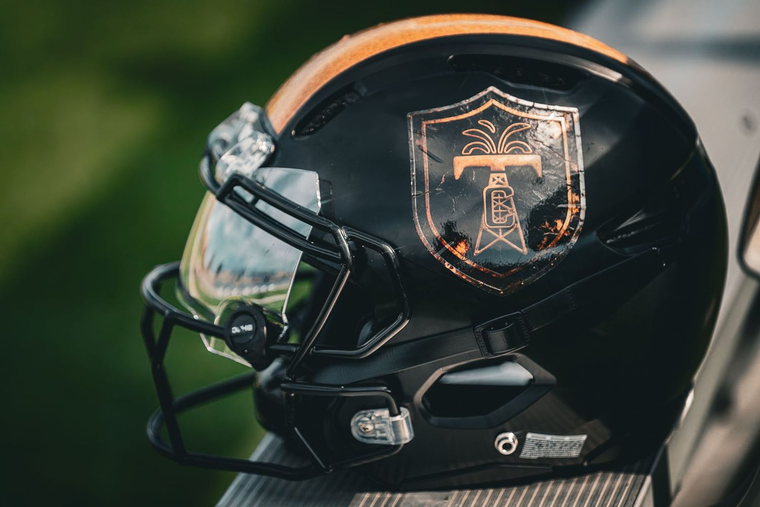 Black football helmet with an oil derrick shield logo rests on a bench in natural light.