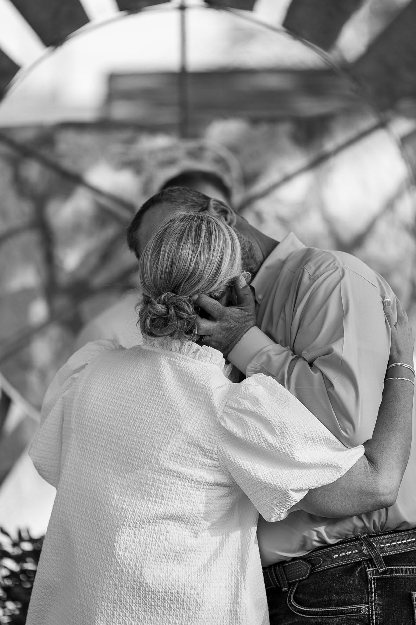 Black and white photo of a couple embracing tenderly, man gently holding womans face in an outdoor setting.