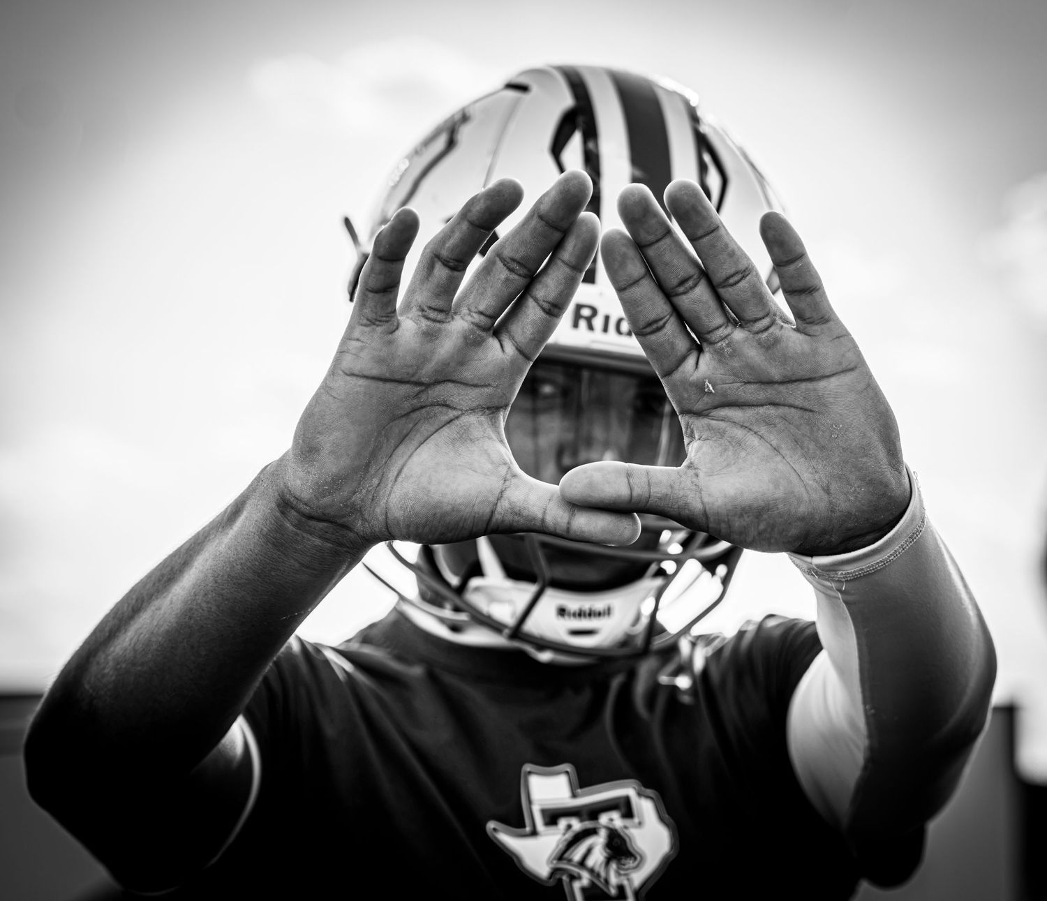 Black and white photo of a football player in helmet making a diamond hand gesture toward the camera.