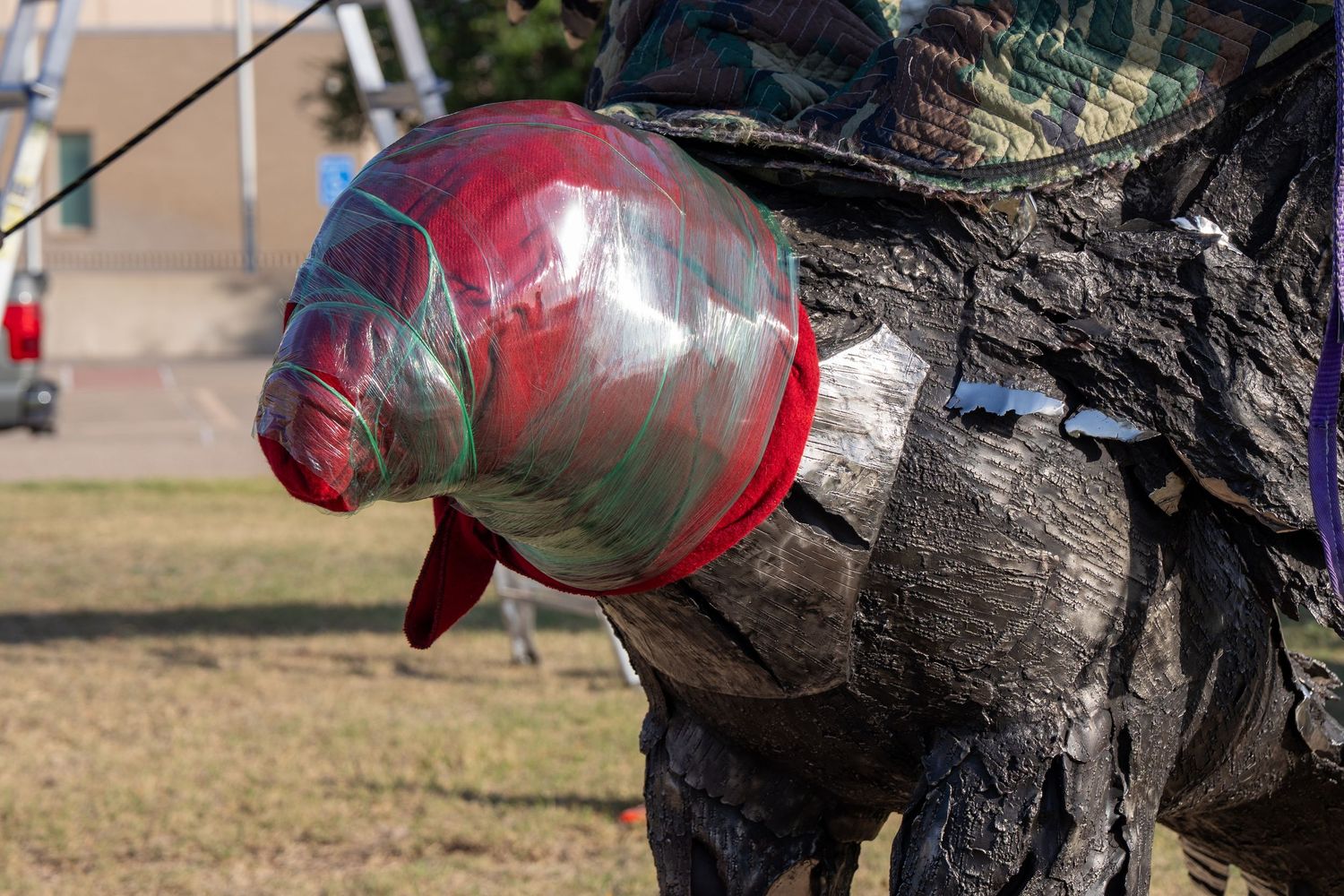 Person in camouflage holding a red and green decorative fish balloon outdoors on a sunny day.
