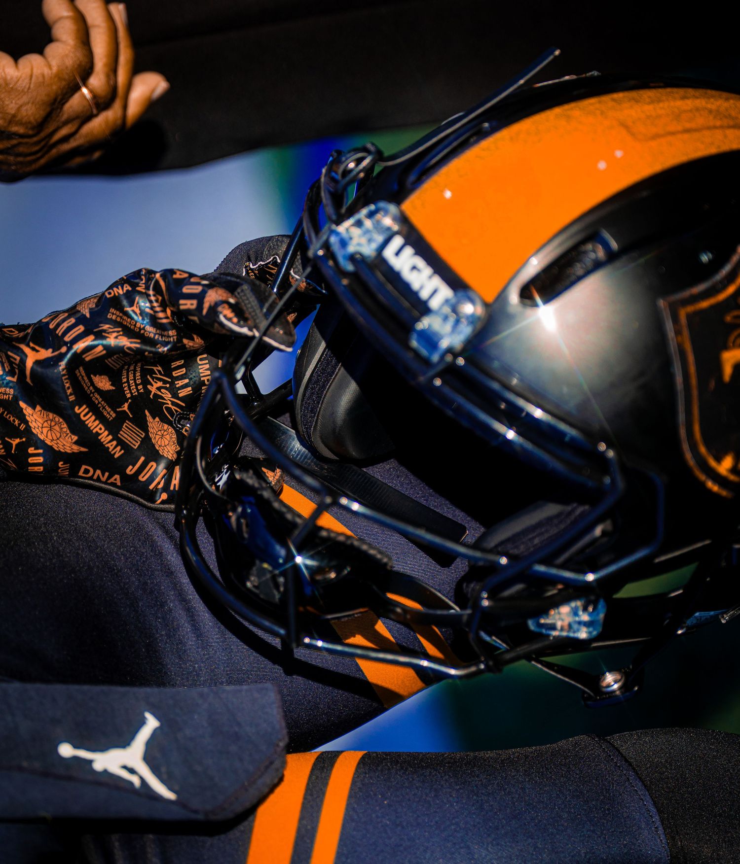 Orange and navy football helmet with visor held by player wearing Jordan brand gloves.