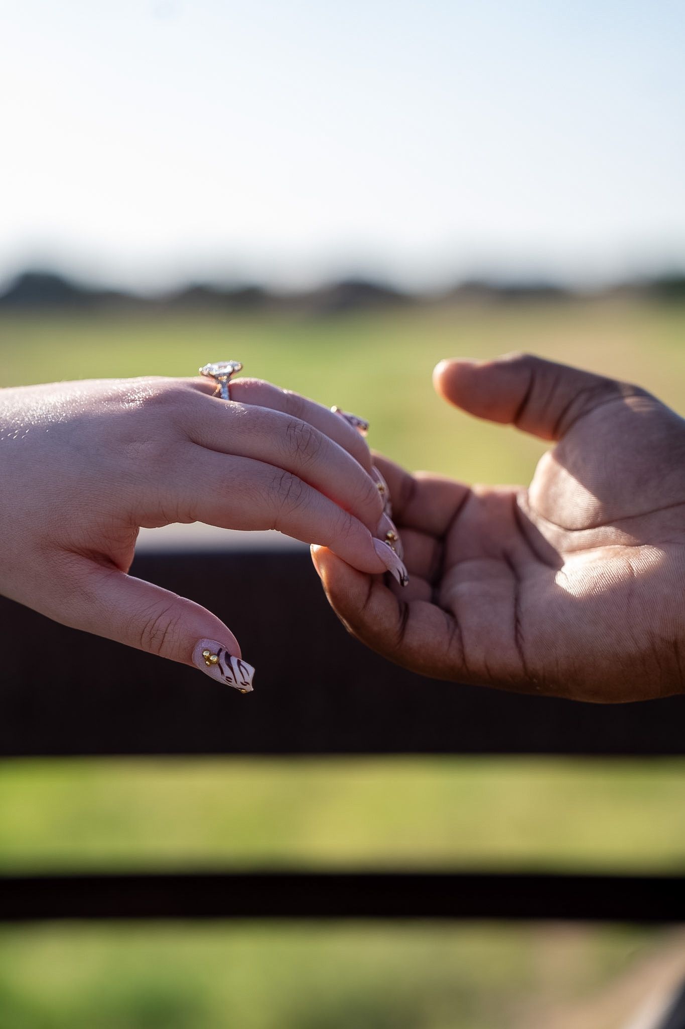 Close-up of couple holding hands with womans marquise diamond engagement ring visible outdoors.