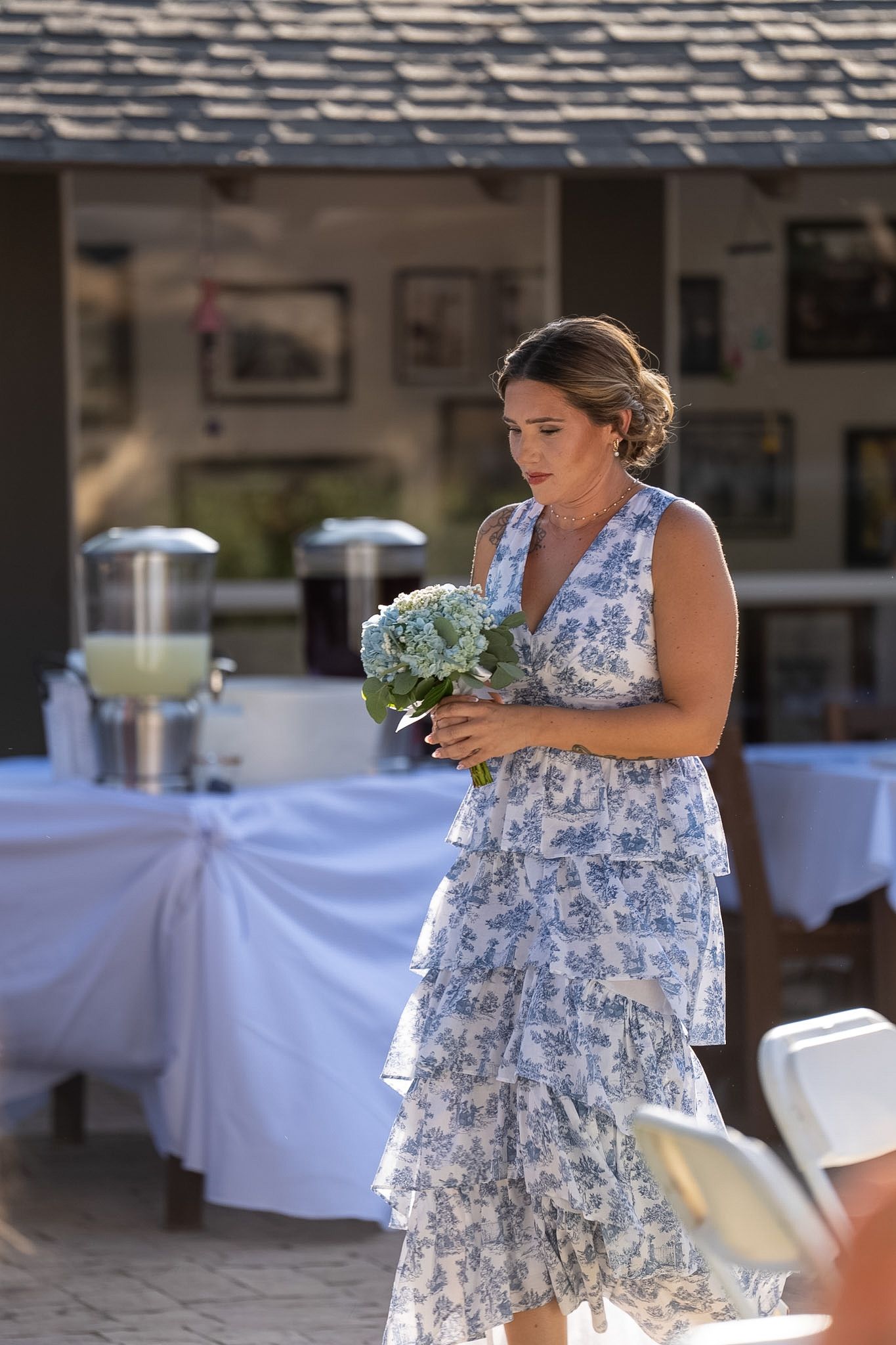 Woman in blue floral dress holding hydrangea bouquet at outdoor wedding reception.