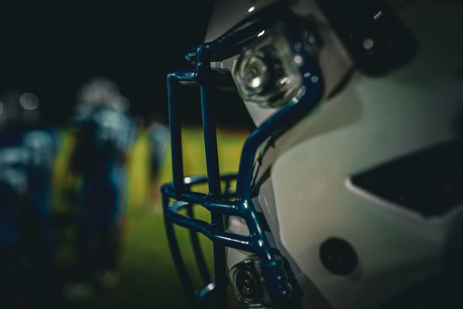 Close-up of a white football helmet with blue face guard under dramatic night lighting on the field.