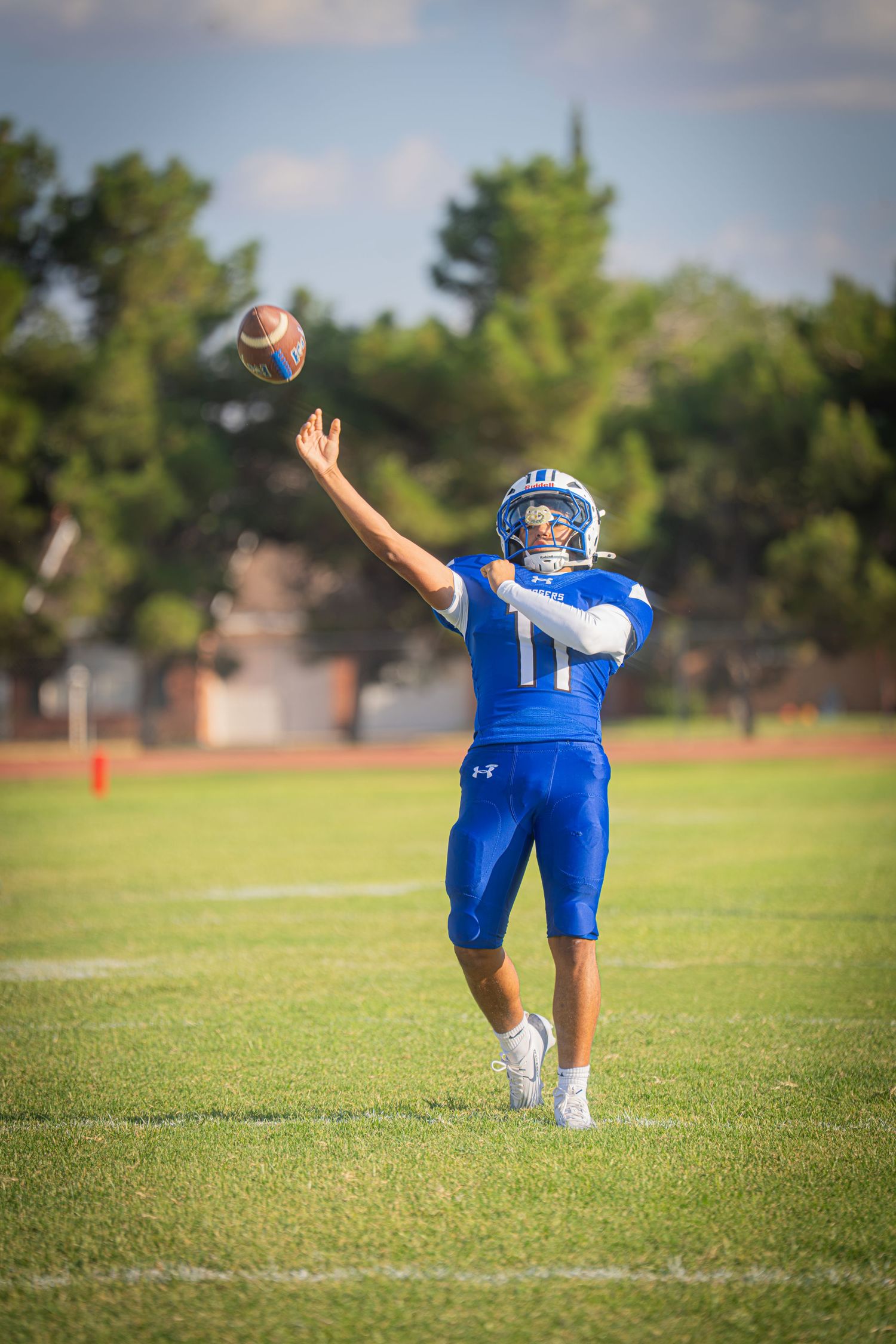 Young football quarterback in blue uniform throwing a pass on a green field during a game.