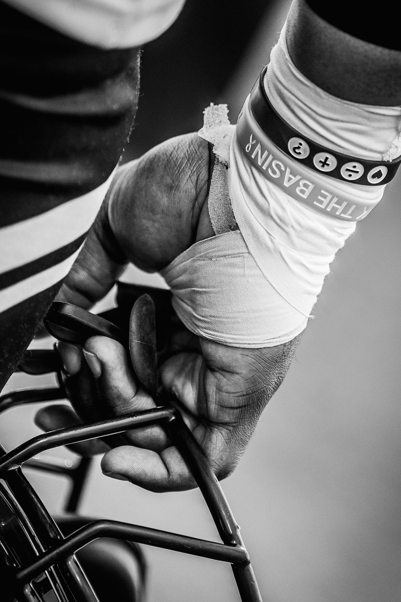 Black and white close-up of a wrapped hand gripping a bicycle handlebar with wristbands.