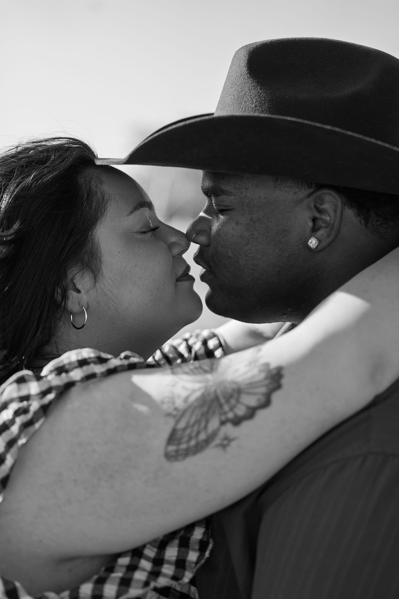 Black and white romantic photo of interracial couple about to kiss, man in cowboy hat.
