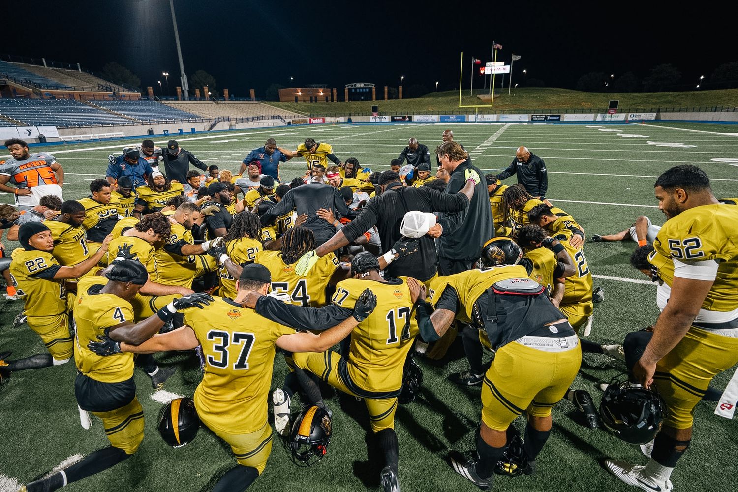 Football team huddles together on field in yellow uniforms after game.