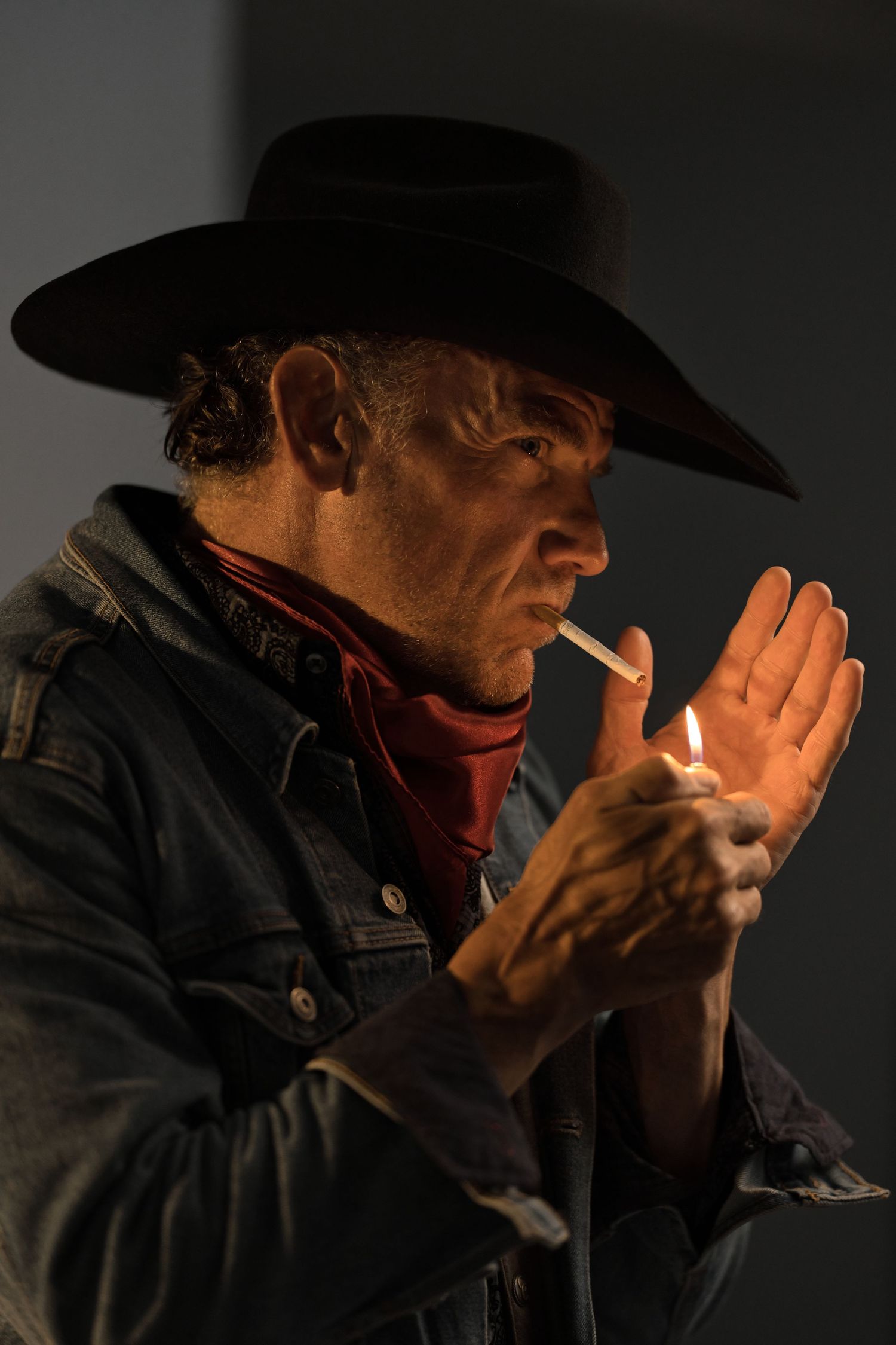 Cowboy lighting a cigarette with a lighter while wearing a black hat and bandana.