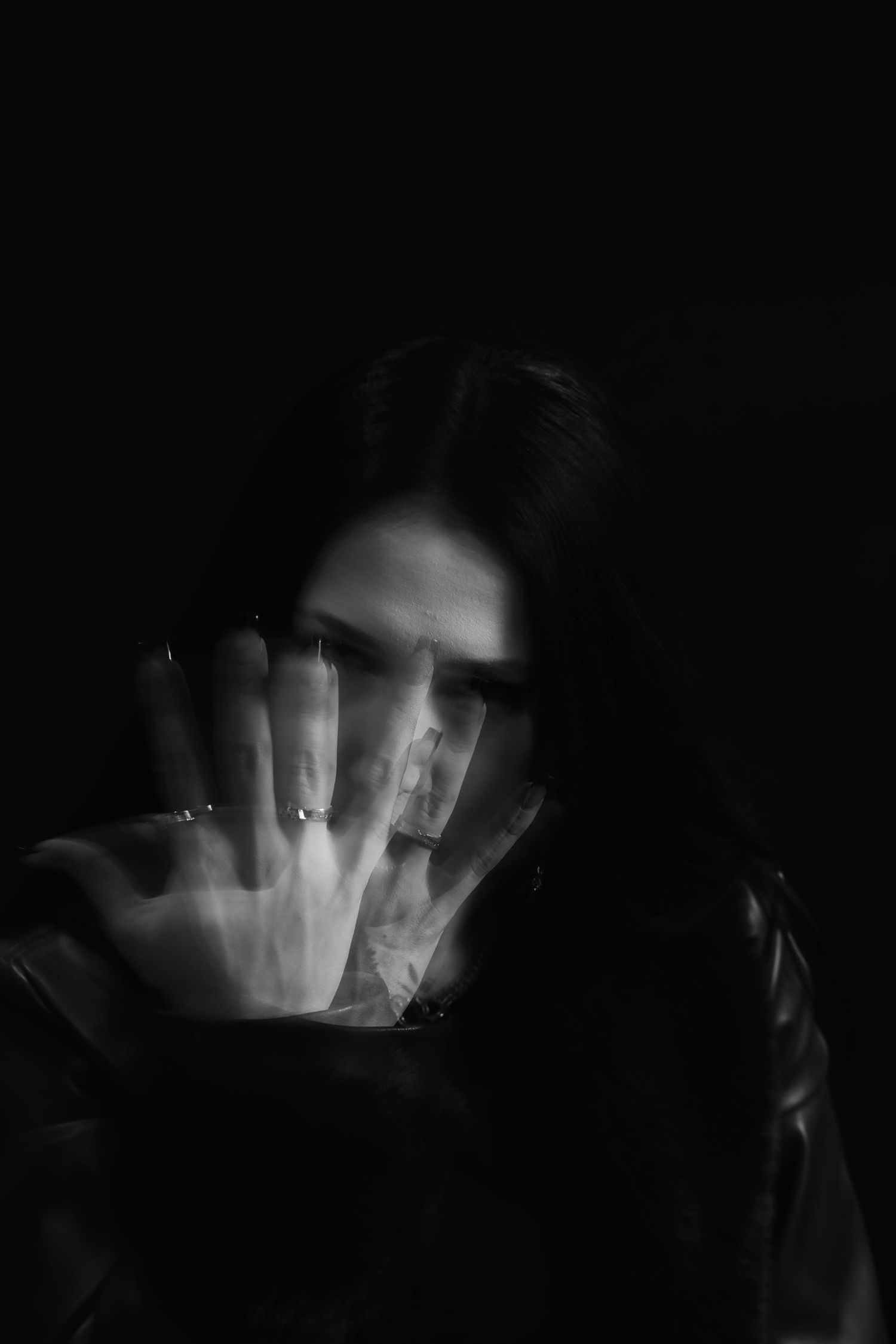 Black and white portrait of woman holding hand up toward camera in dramatic low-key lighting.