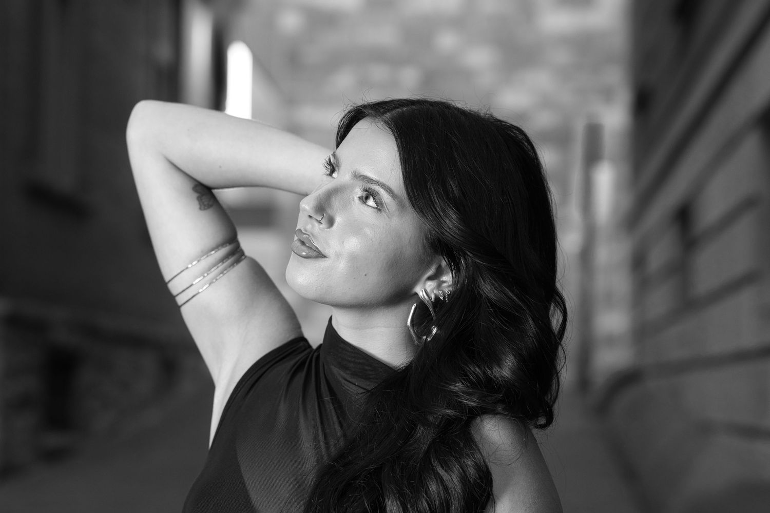 Black and white portrait of a woman with long dark hair posing gracefully in an urban alley.