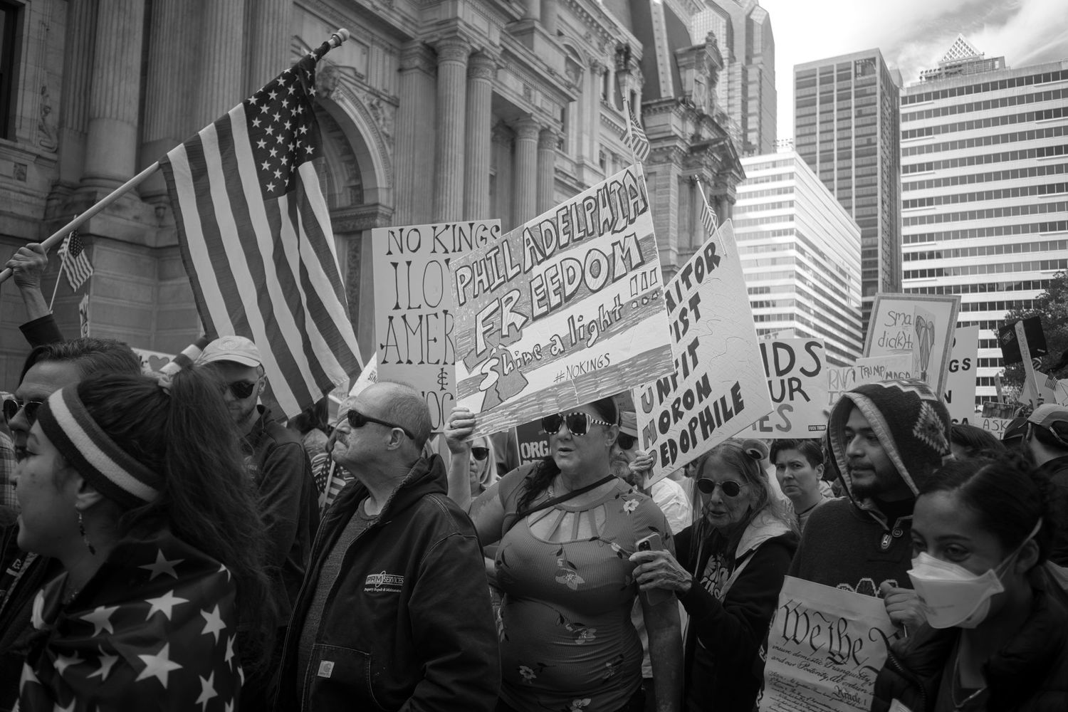 Black and white photo of protesters holding American flags and signs at a political rally or demonstration.