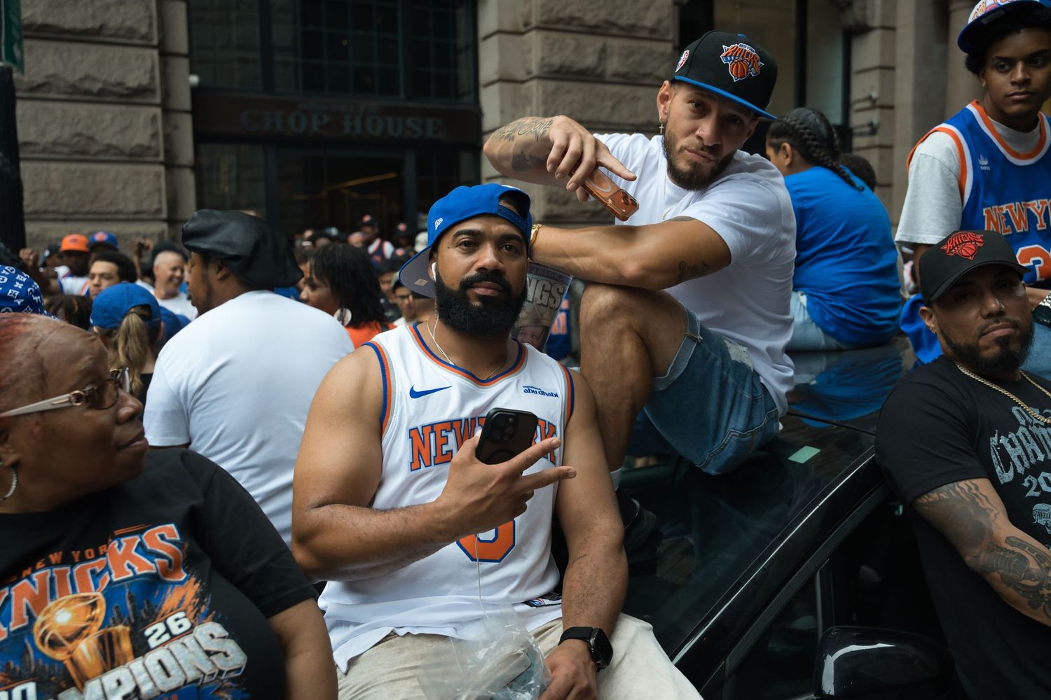 New York Knicks fans celebrate at a parade, wearing team jerseys and hats in blue and orange.