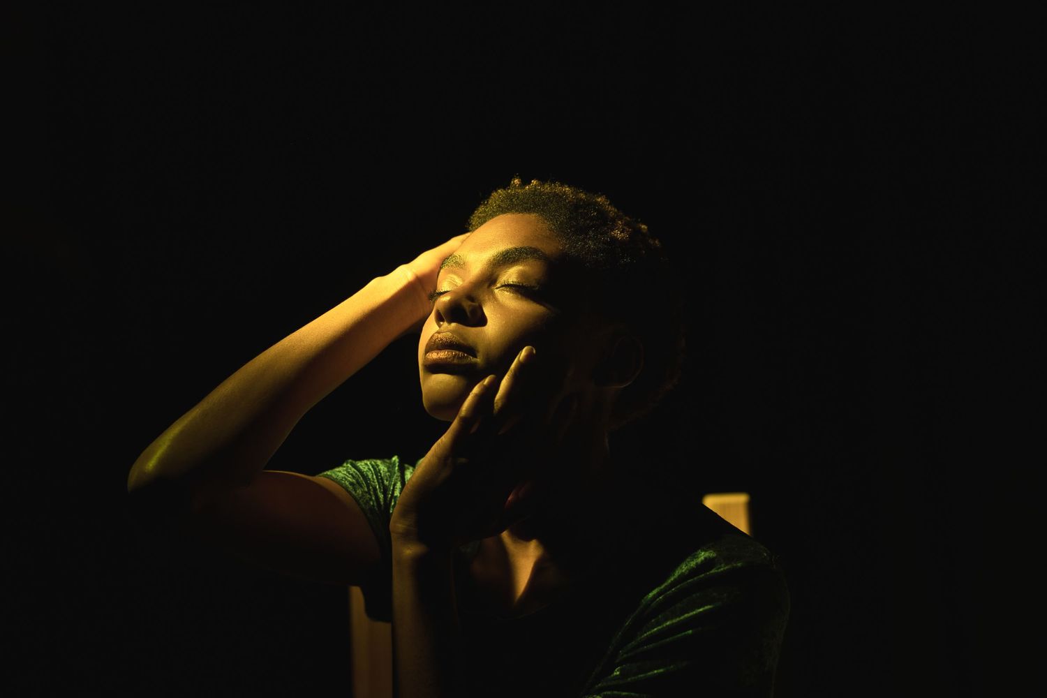 Dramatic portrait of person with hand on face illuminated by warm yellow stage light.