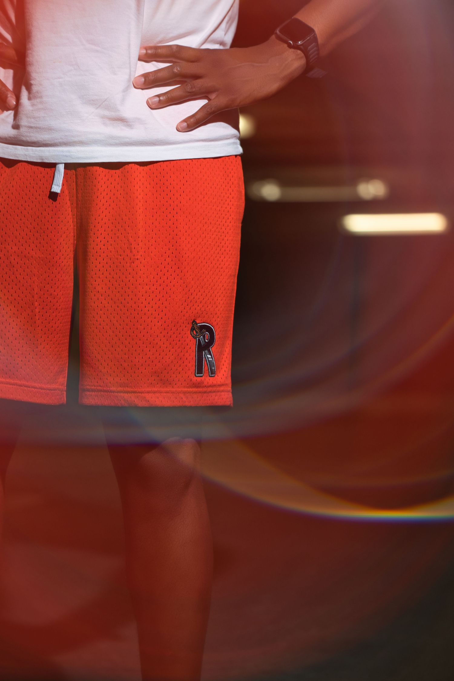 Close-up of a person wearing red mesh basketball shorts with a letter R logo.