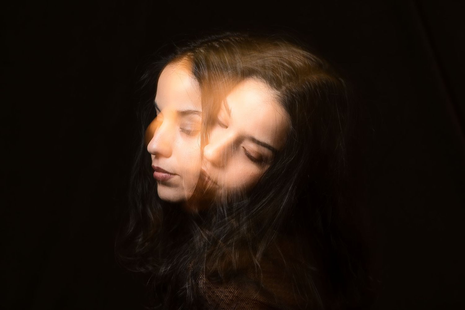 Double exposure portrait of a woman with long dark hair on black background.