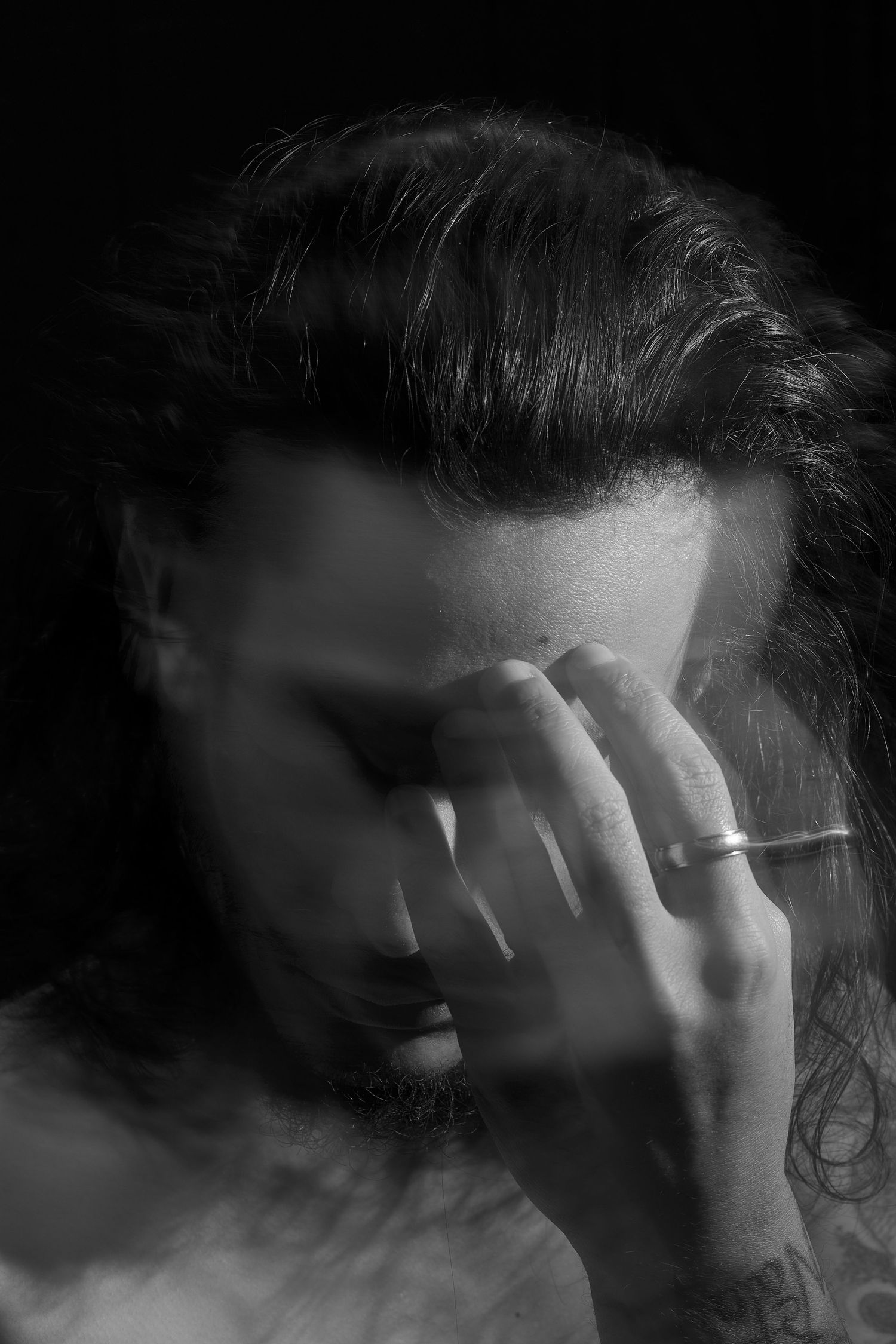 Black and white portrait of person covering face with hand in emotional pose.