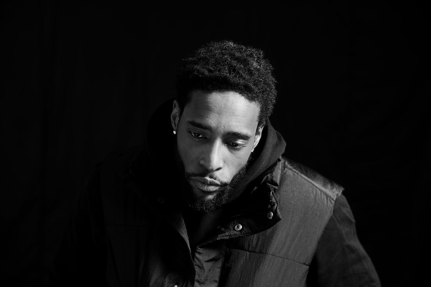 Black and white portrait of a young Black man in puffer jacket with serious expression.