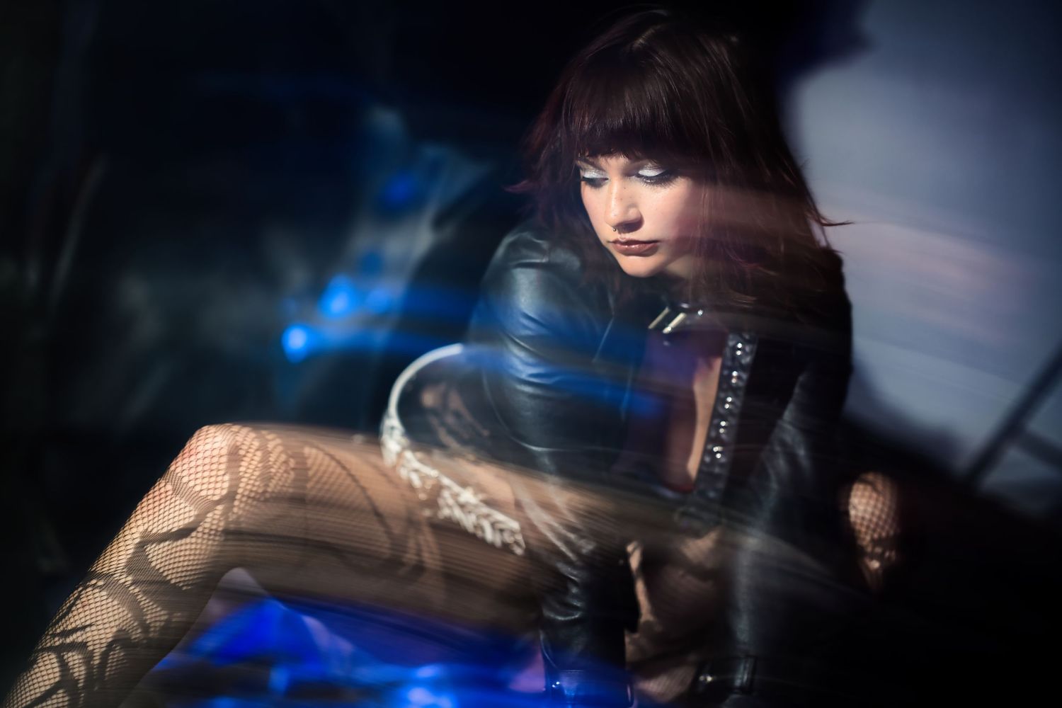 Woman in a leather jacket and fishnet tights posed dramatically with blue and purple light effects.