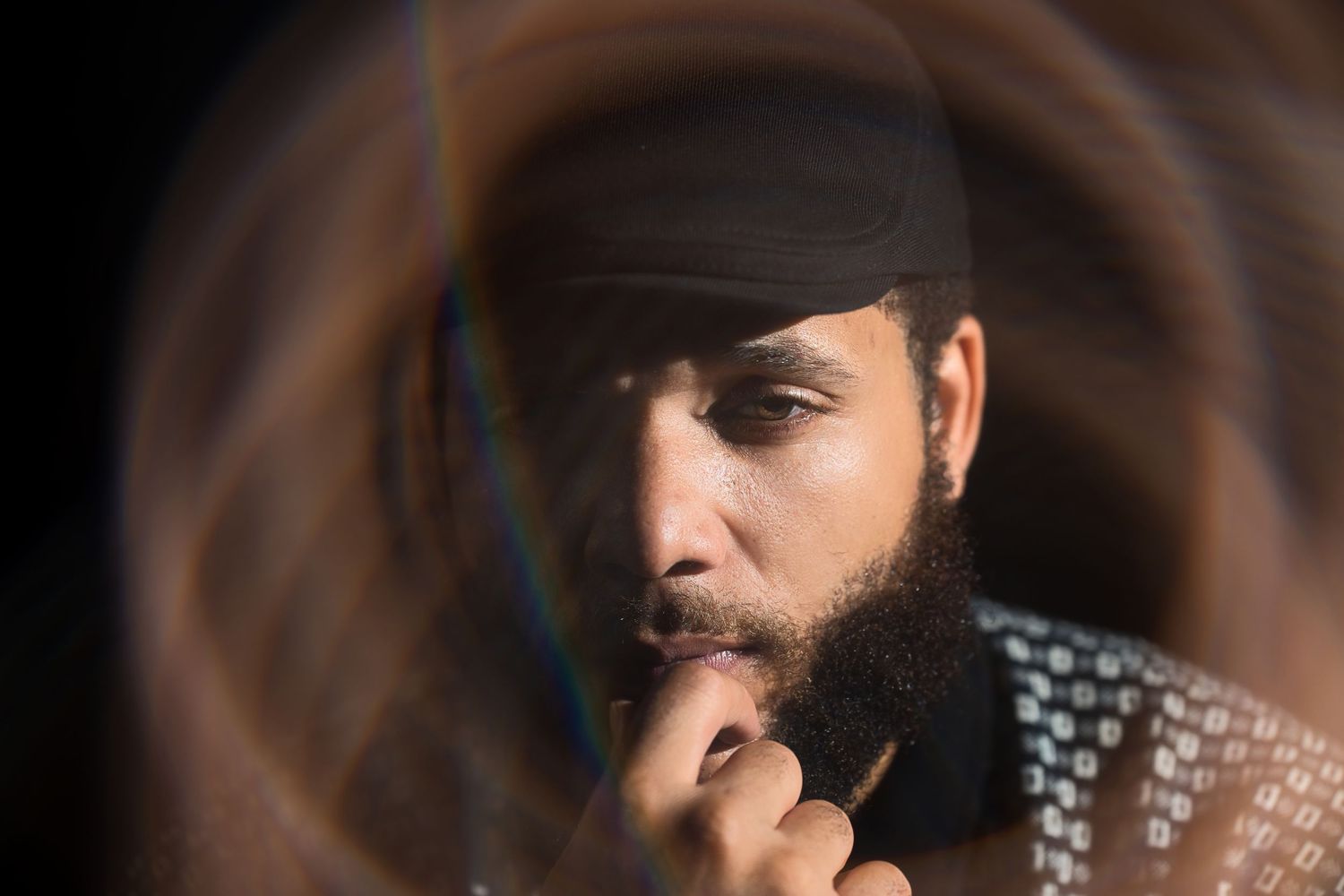 Bearded man in black turban reflected in a circular mirror with blurred hair in the foreground.