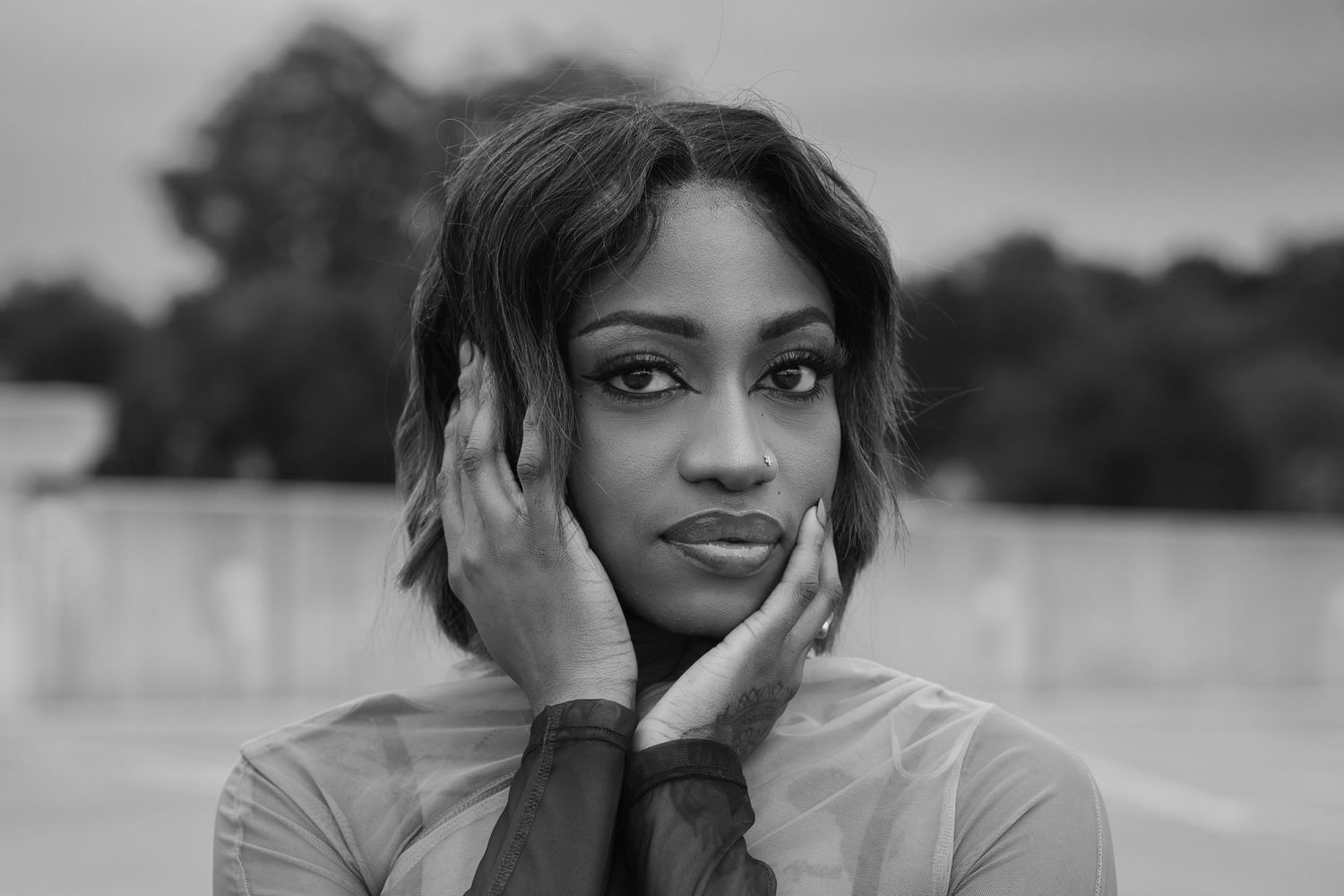 Black and white portrait of young woman with hands on cheeks outdoors.