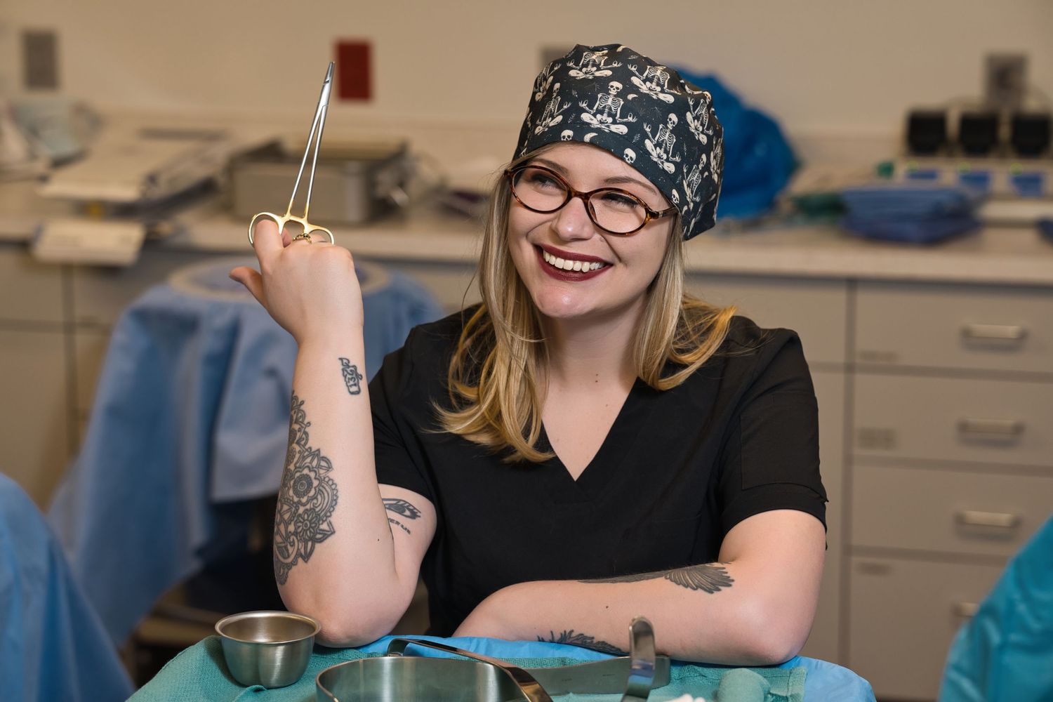 Smiling female medical professional in scrub cap holding surgical instrument in operating room.