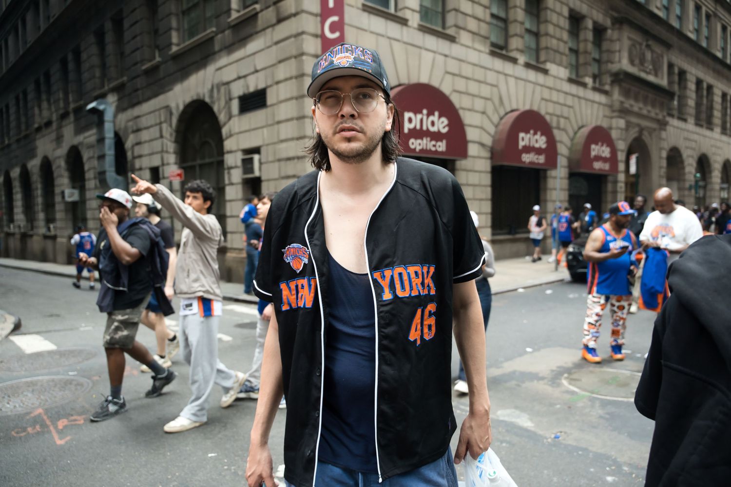 Man wearing New York Knicks jersey number 46 standing on a busy city street during an outdoor event.