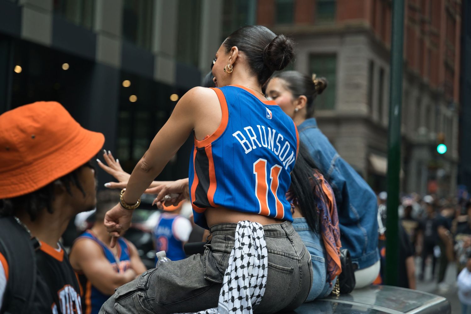Woman wearing Brunson New York Knicks jersey at outdoor street parade celebration.
