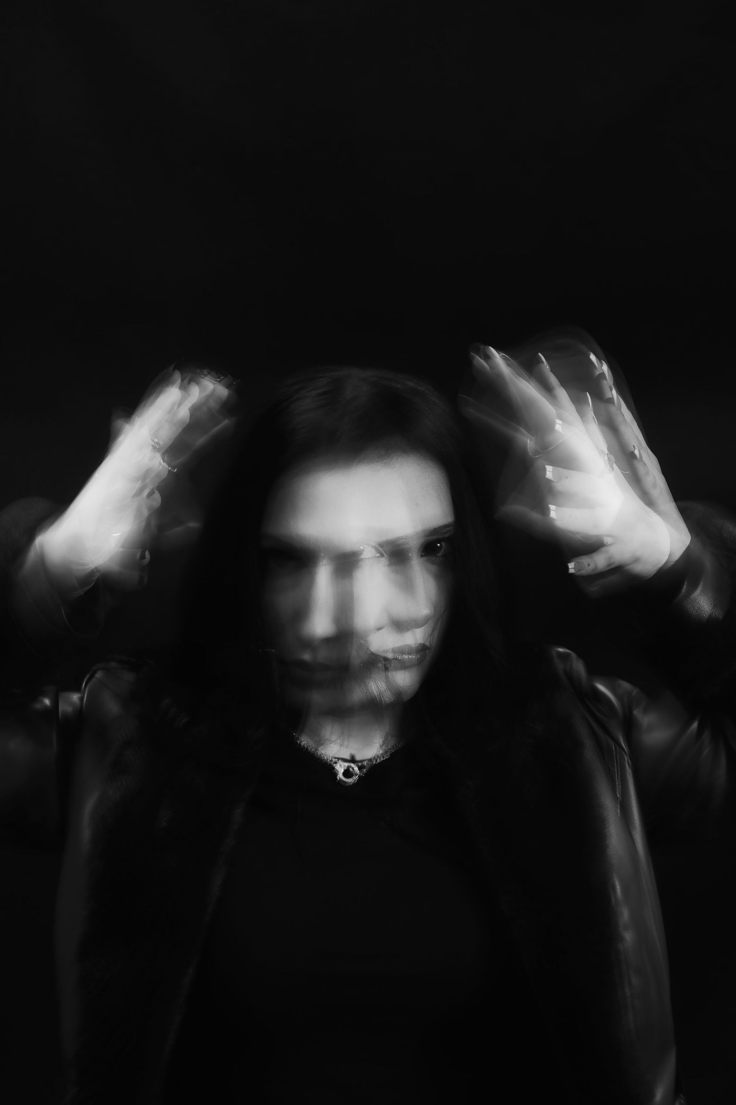 Black and white blurred portrait of a person with raised hands and long dark hair.