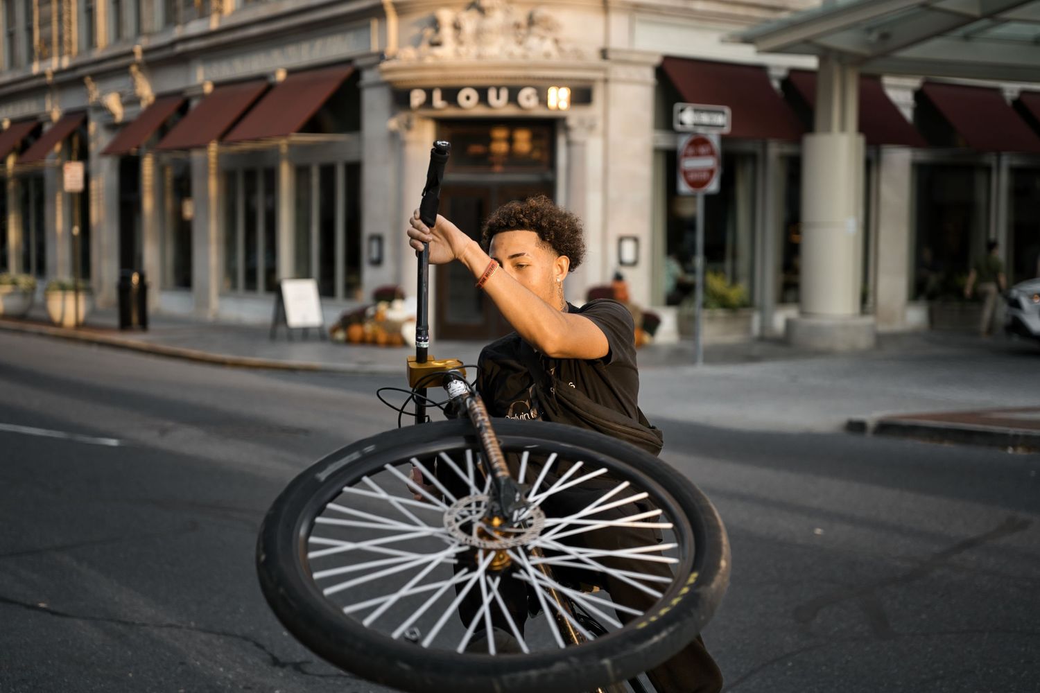 Young man performing a BMX bike trick on a city street, holding a bicycle wheel aloft near a historic building.