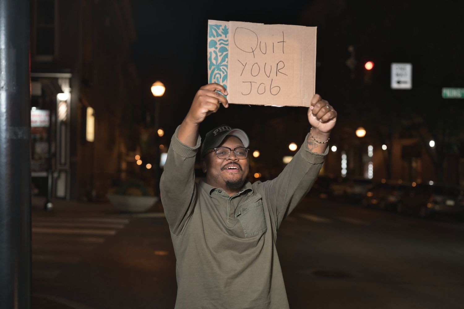 Man holding 'Quit Your Job' cardboard sign on urban street corner at night.
