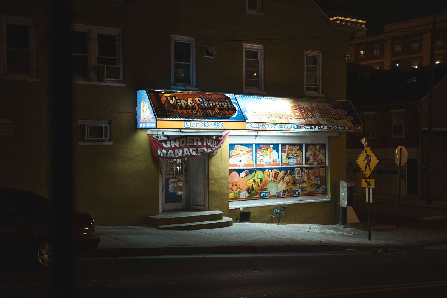 A small corner store glowing with neon signs at night in an urban neighborhood.