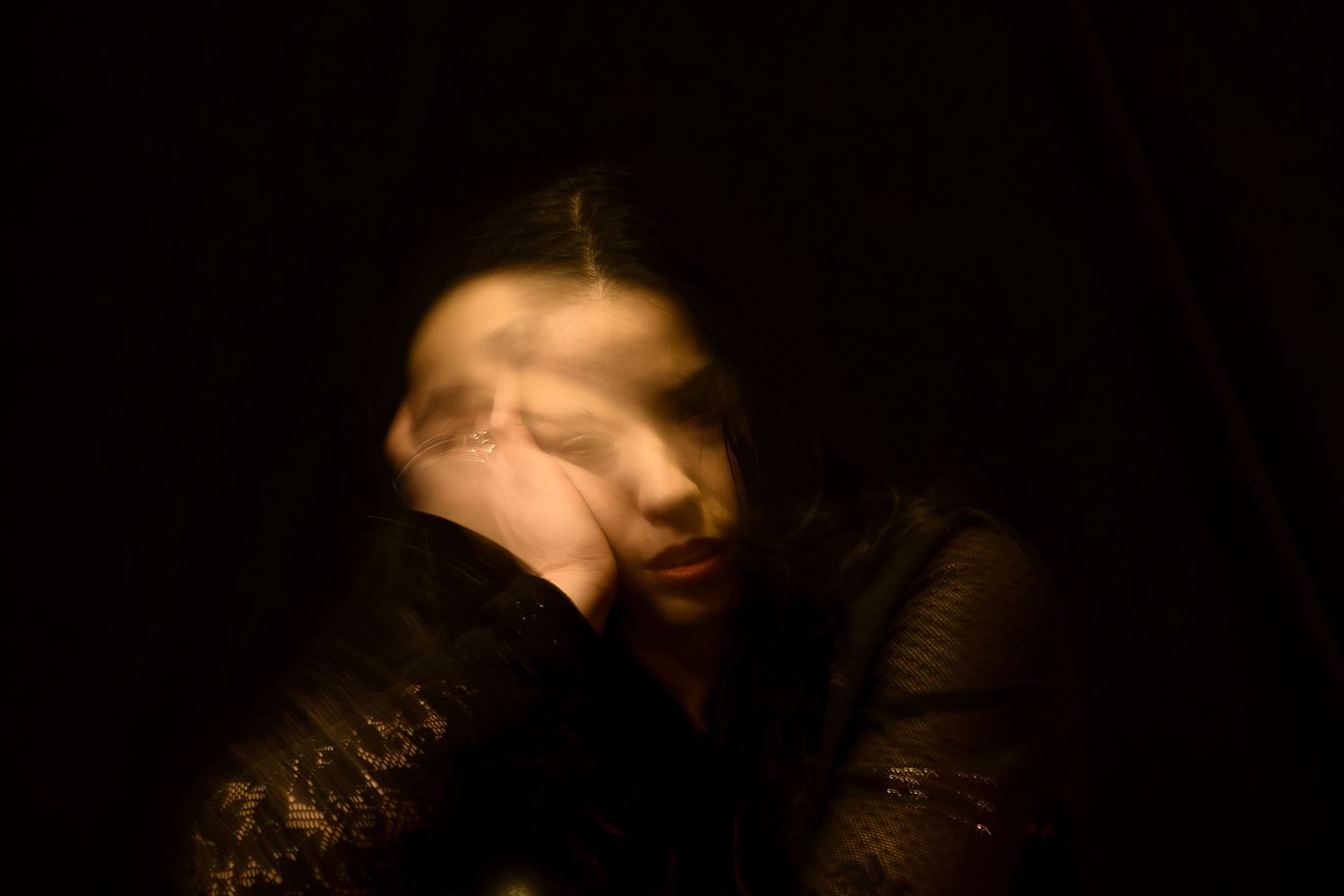 Artistic long exposure portrait of a person in dark jacket against black background.