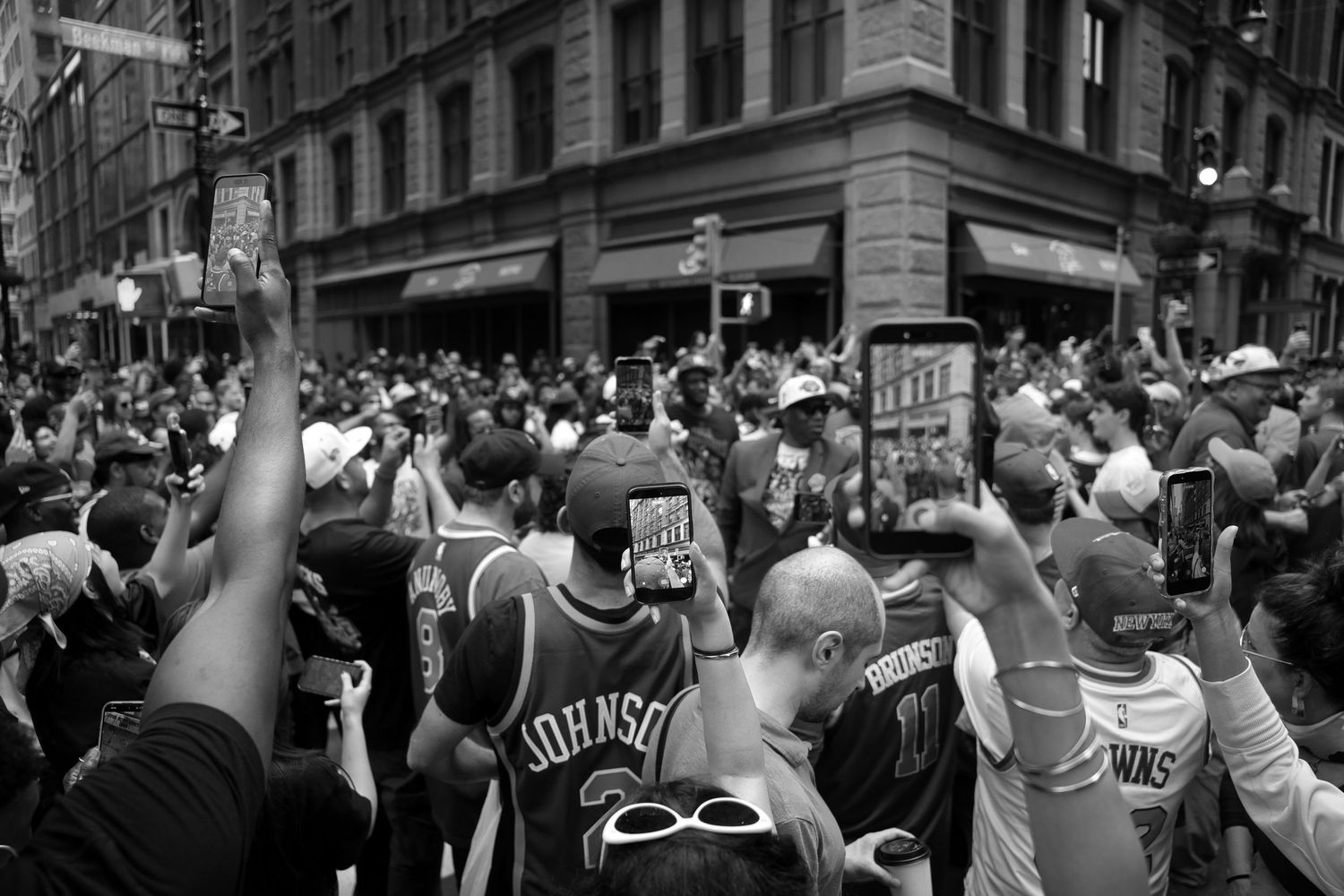 Black and white photo of a large crowd at an NBA parade, fans wearing basketball jerseys and filming with phones.