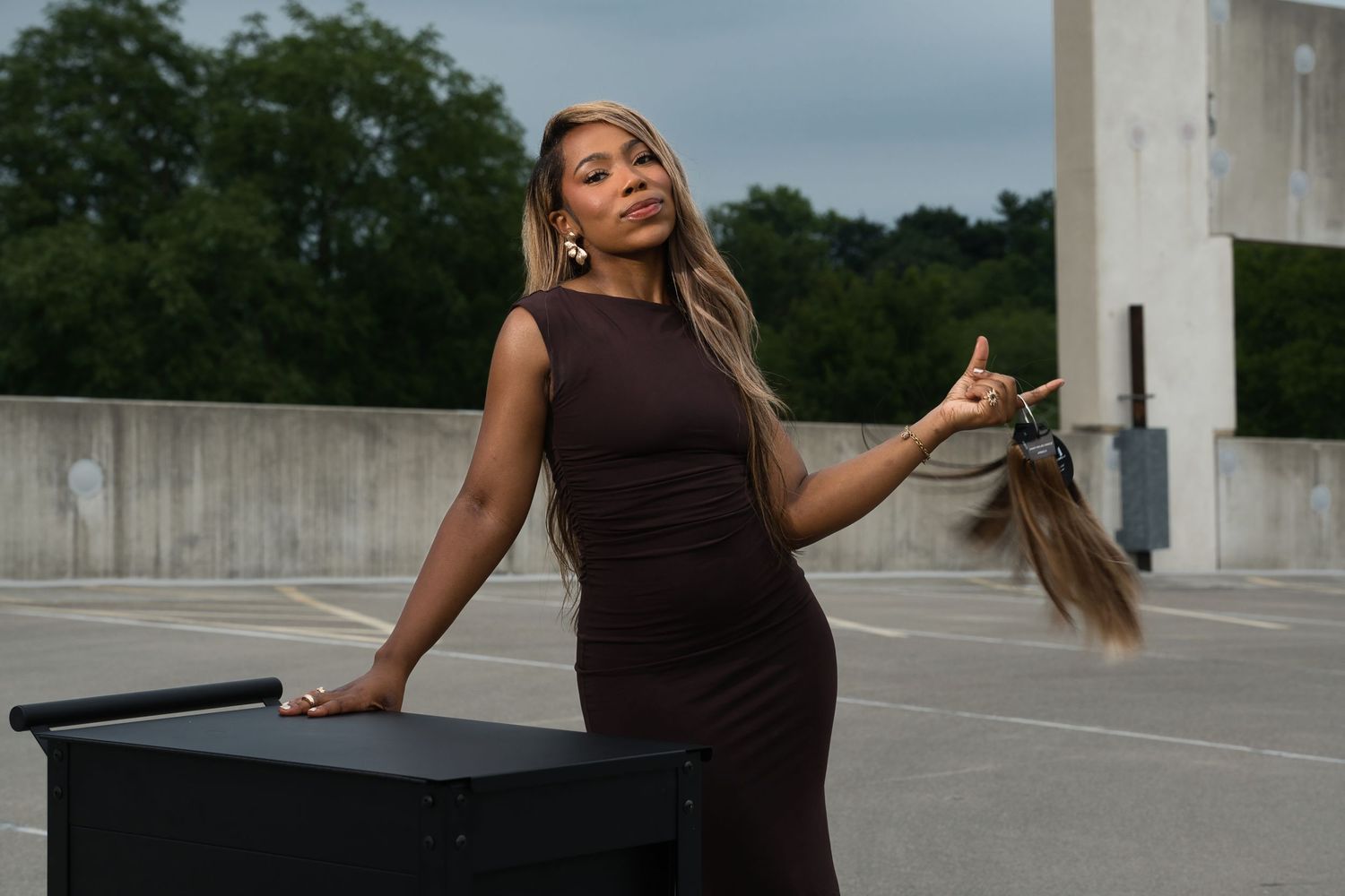 Woman in a brown dress posing with long hair extensions on a rooftop parking lot.