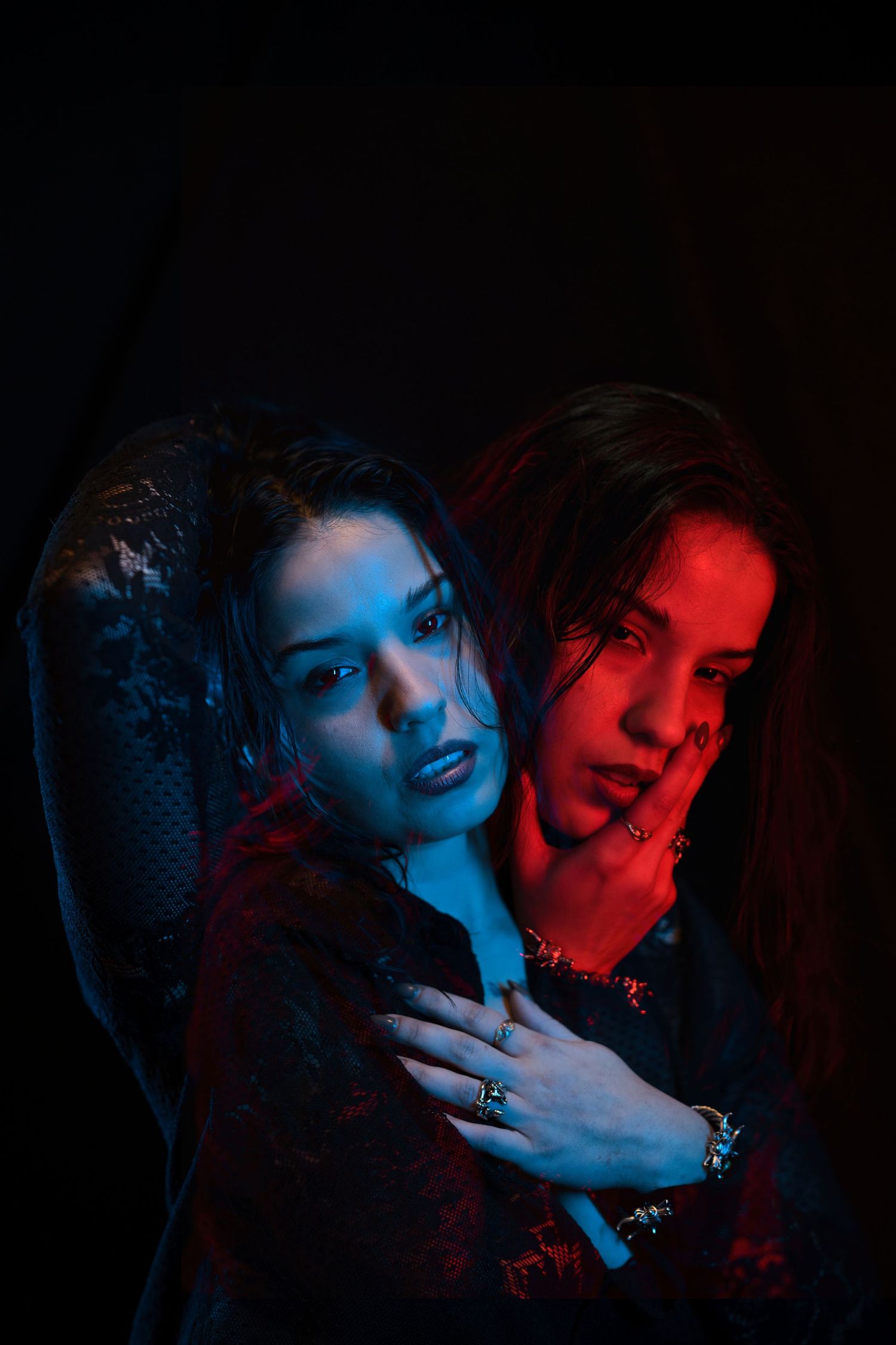 Two women posed together under dramatic blue and red lighting on dark background.