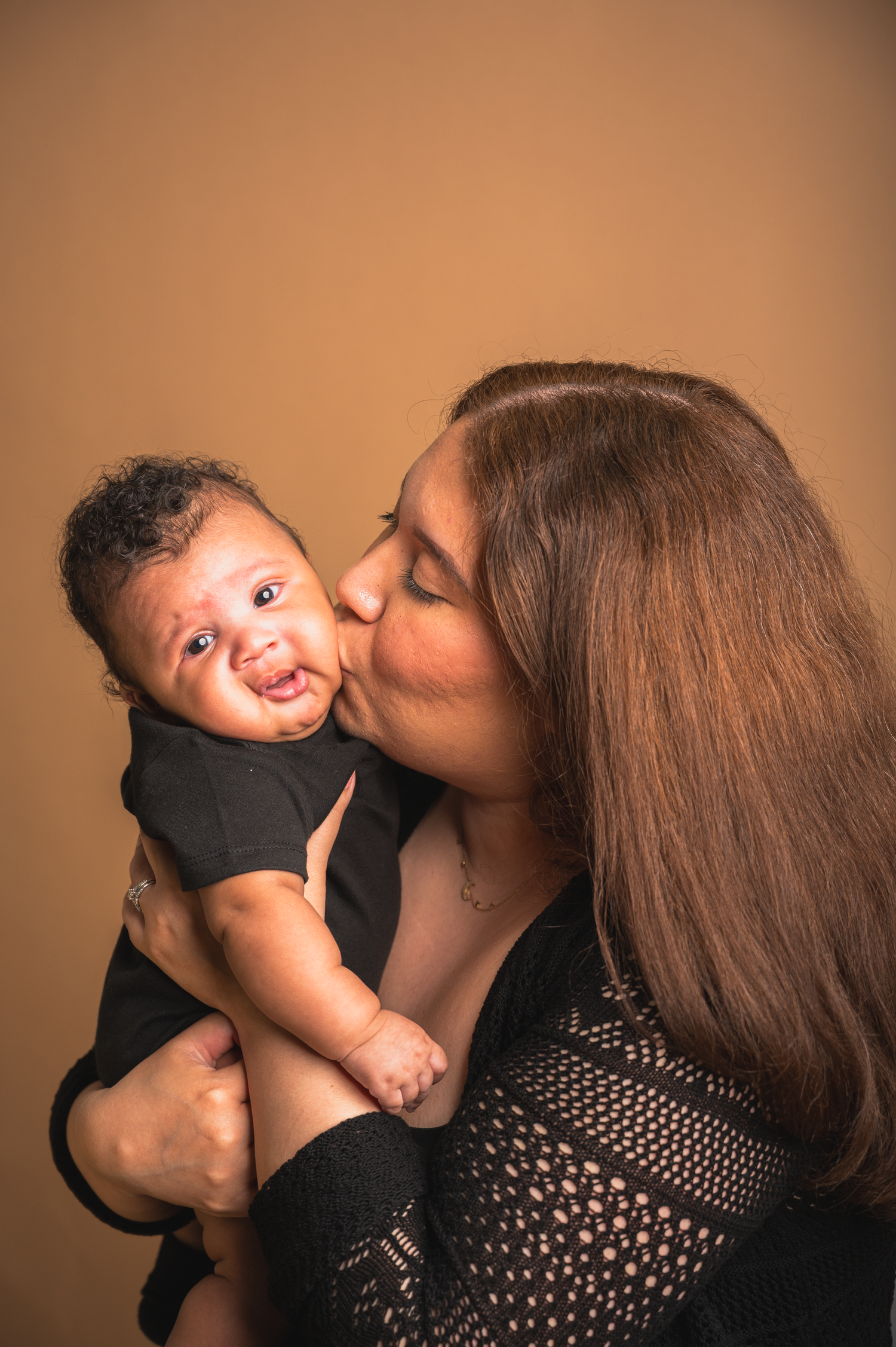 Mother kissing
 her newborn baby in a studio portrait session.