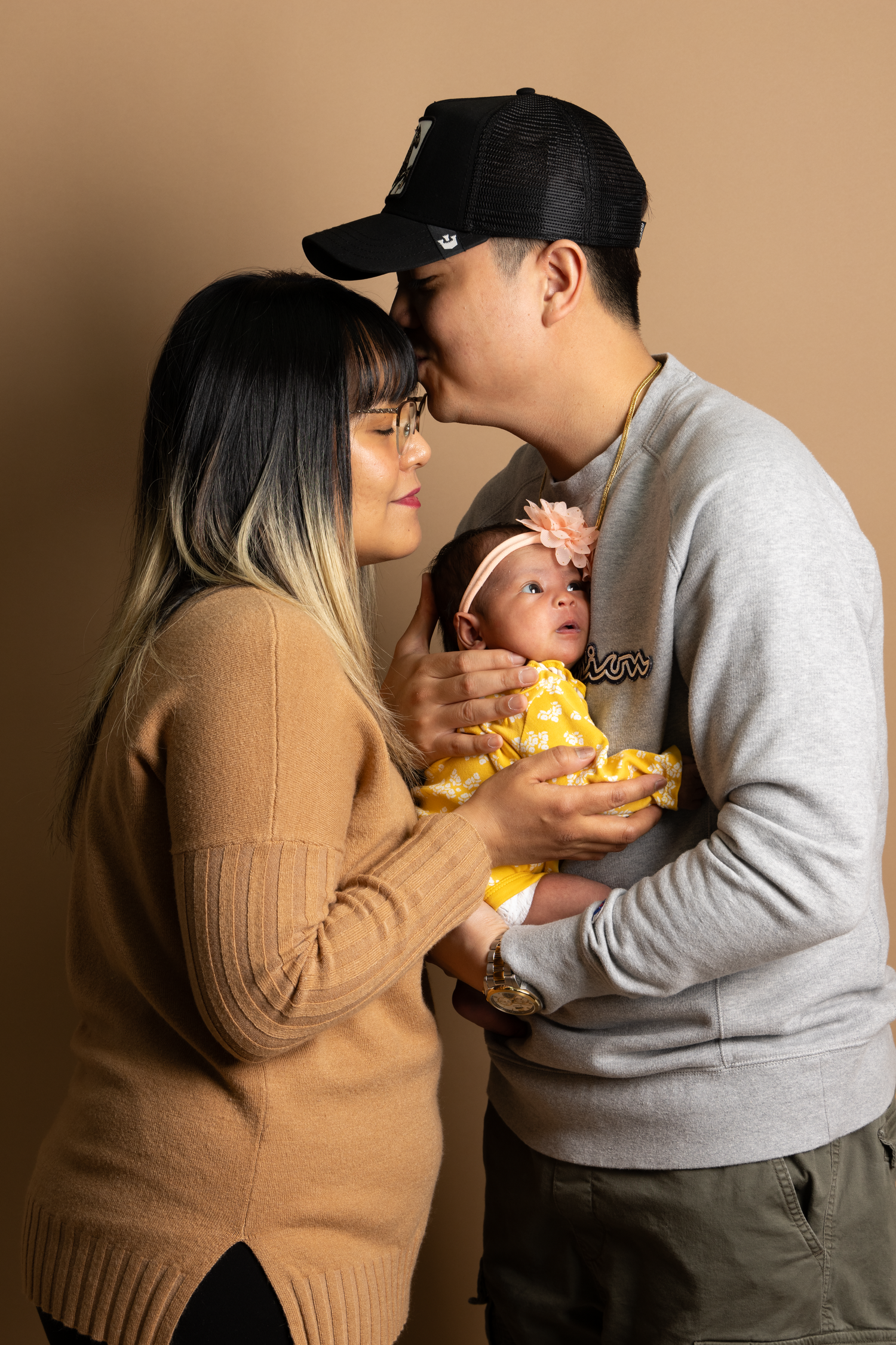 Parents holding their newborn baby in a studio portrait session. Dad kissing mom on the forehead.