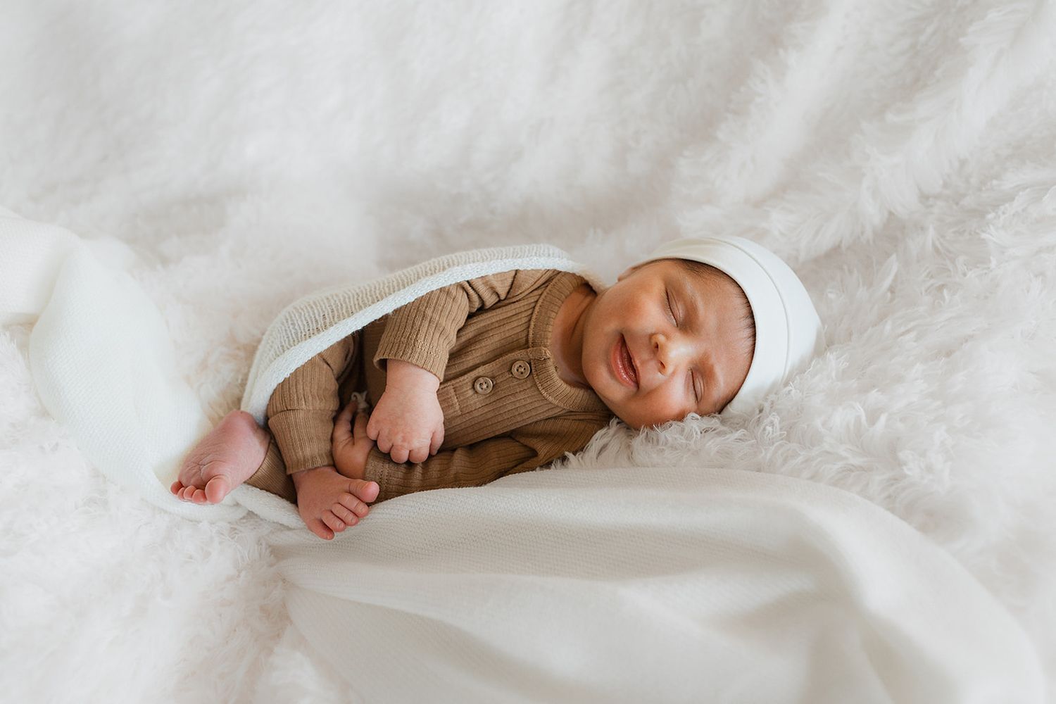 A newborn baby's tiny feet and toes wrapped in soft white blankets on a plush surface.