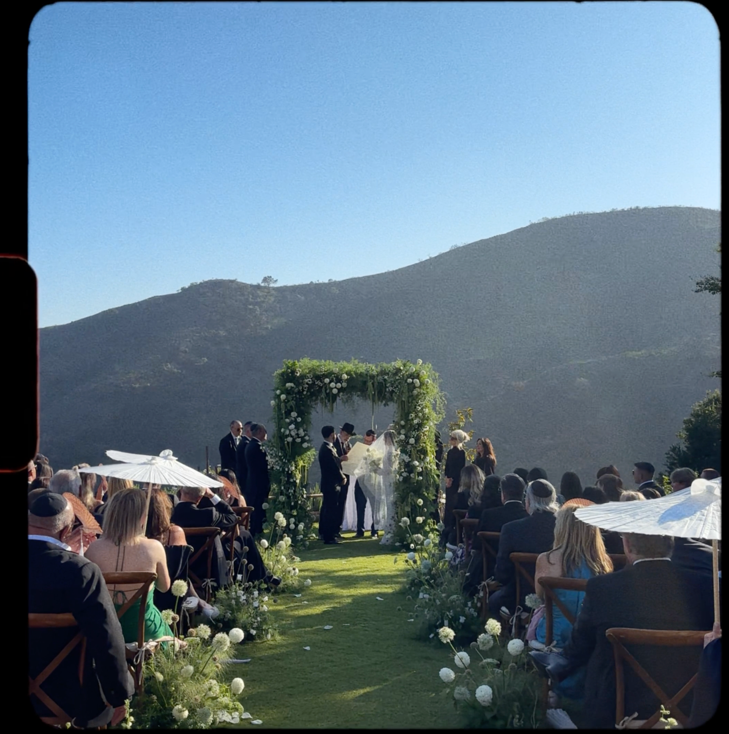 Outdoor wedding ceremony setup with white chairs and floral arrangements against a scenic mountain backdrop.