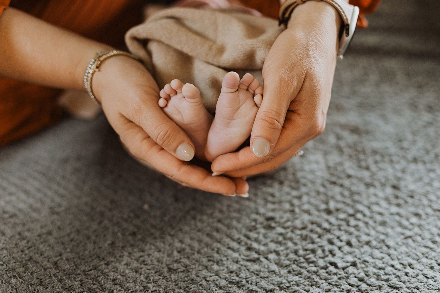Close-up of hands holding a small newborn baby's feet against a gray textured blanket background.