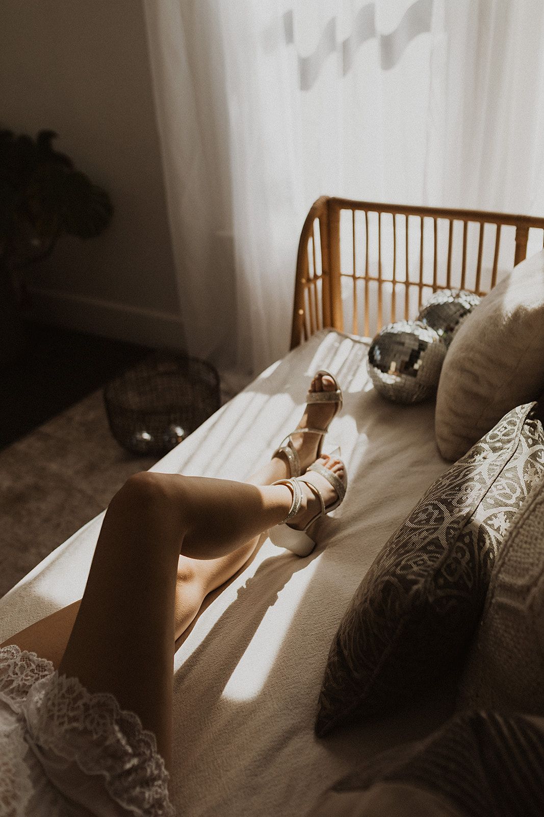 Sunlight streams through curtains onto a cozy bed with decorative pillows and a sleeping cat in warm sepia tones.