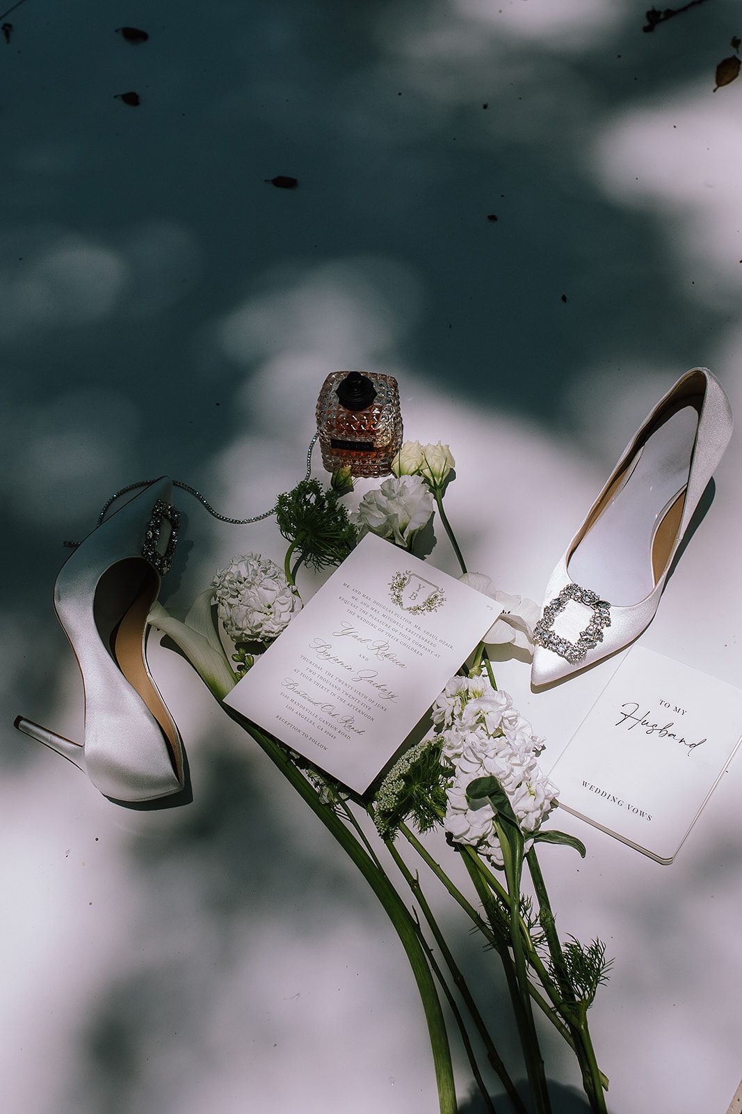 White wedding invitation cards and elegant high heel shoes arranged artistically with delicate floral elements.