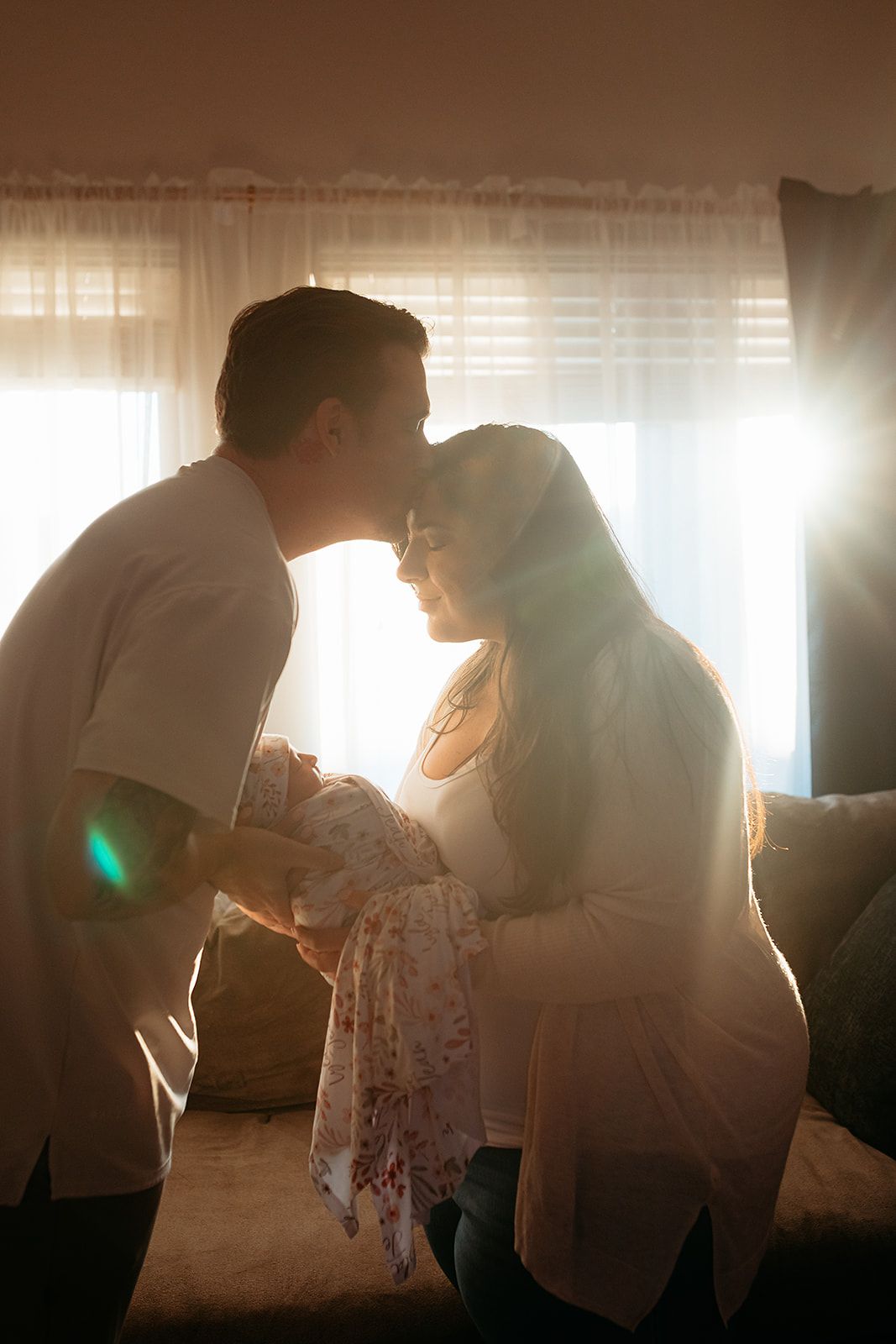 Silhouetted couple sharing an intimate moment in sunlit room with sheer curtains creating romantic ambiance.