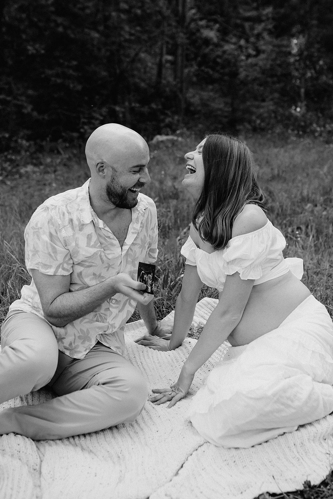 A romantic couple lounges on a white blanket outdoors sharing intimate moments in a black and white photo series.
